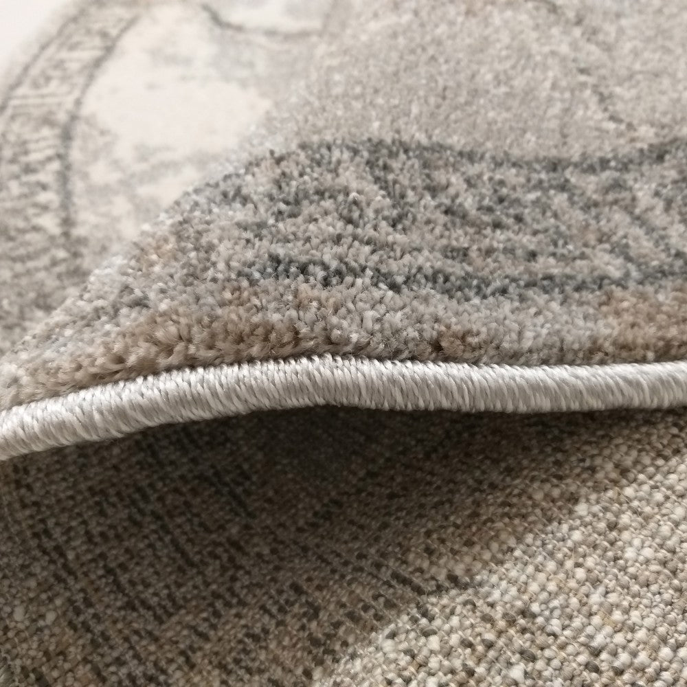 Gros plan sur un tapis en fibres grises et beiges à poil doux, montrant une bordure surpiquée et un léger motif abstrait