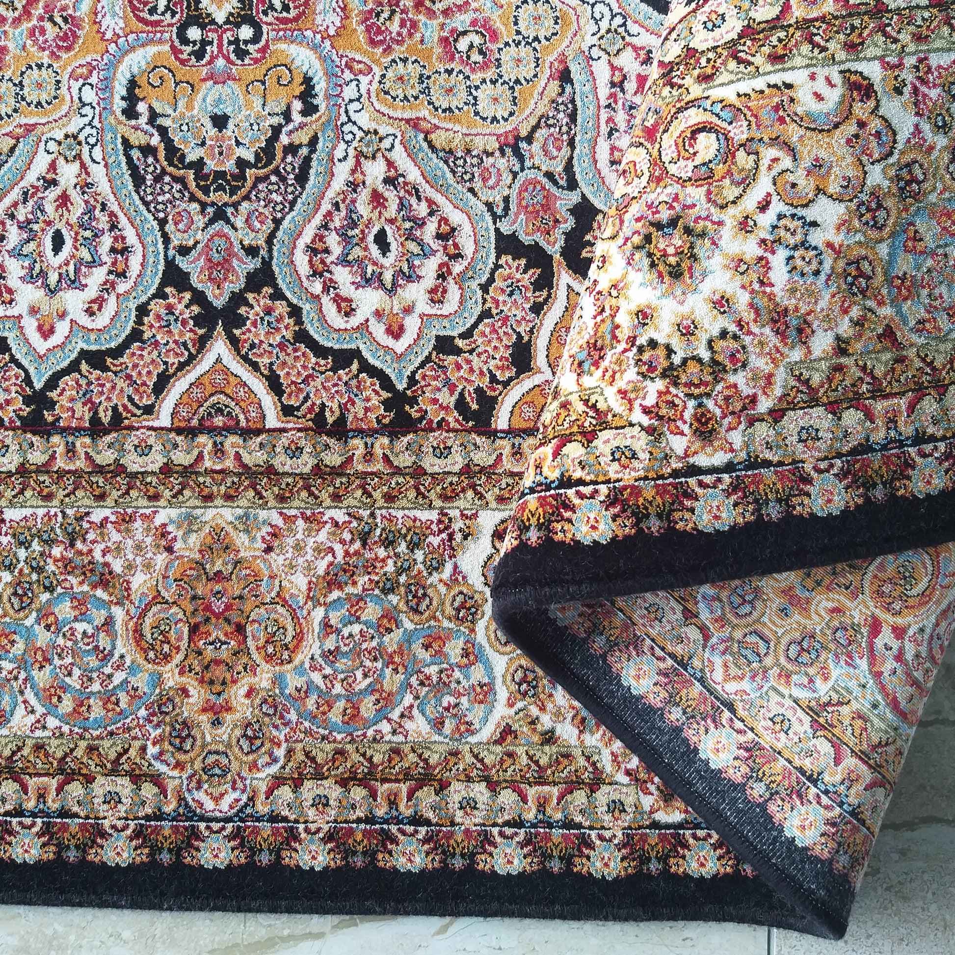 Tapis coloré à motifs floraux et cachemire roulé sur le côté, avec des teintes de noir, crème, rouge, orange et bleu