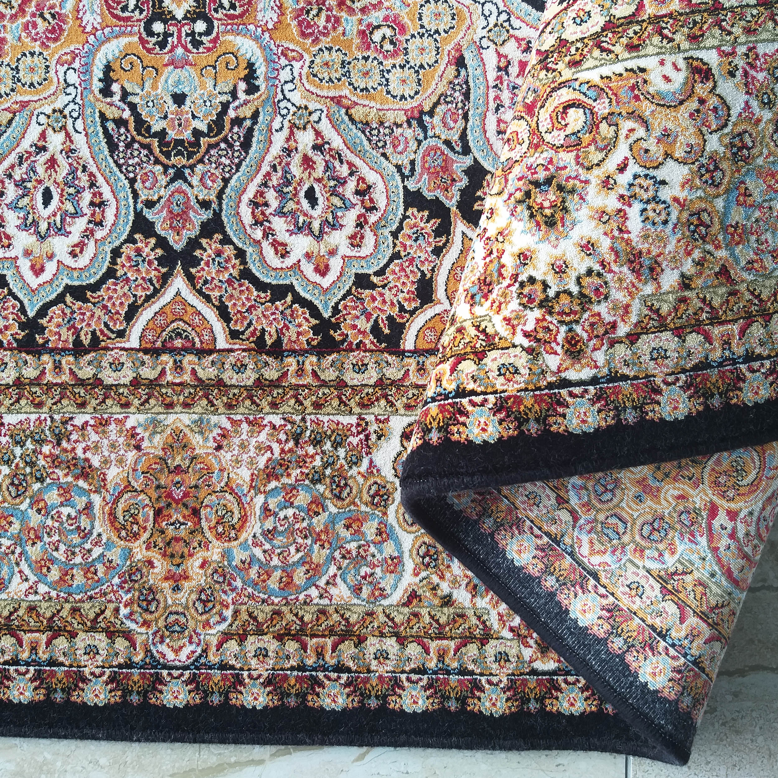 Tapis coloré à motifs floraux et cachemire roulé sur le côté, avec des teintes de noir, crème, rouge, orange et bleu