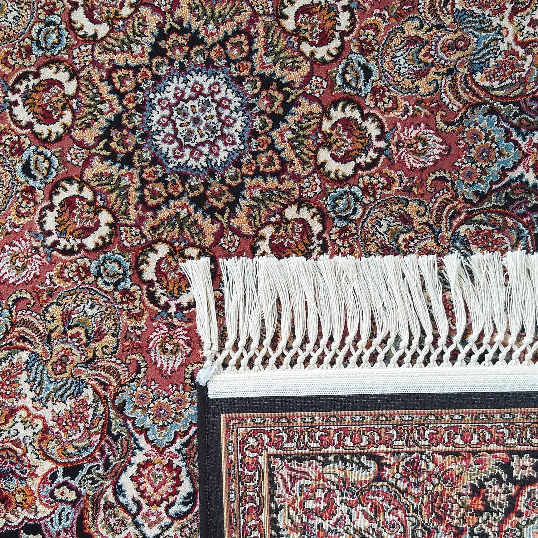 Tapis avec un motif floral ornemental en rouge, noir, crème et bleu, doté de franges blanches nettes