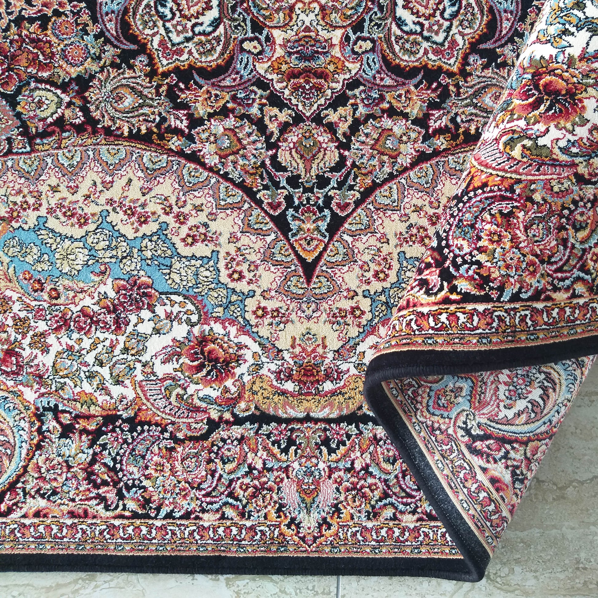 Tapis à motifs floraux et cachemire complexes, rouge, or, bleu et crème sur fond noir, partiellement roulé sur un sol clair