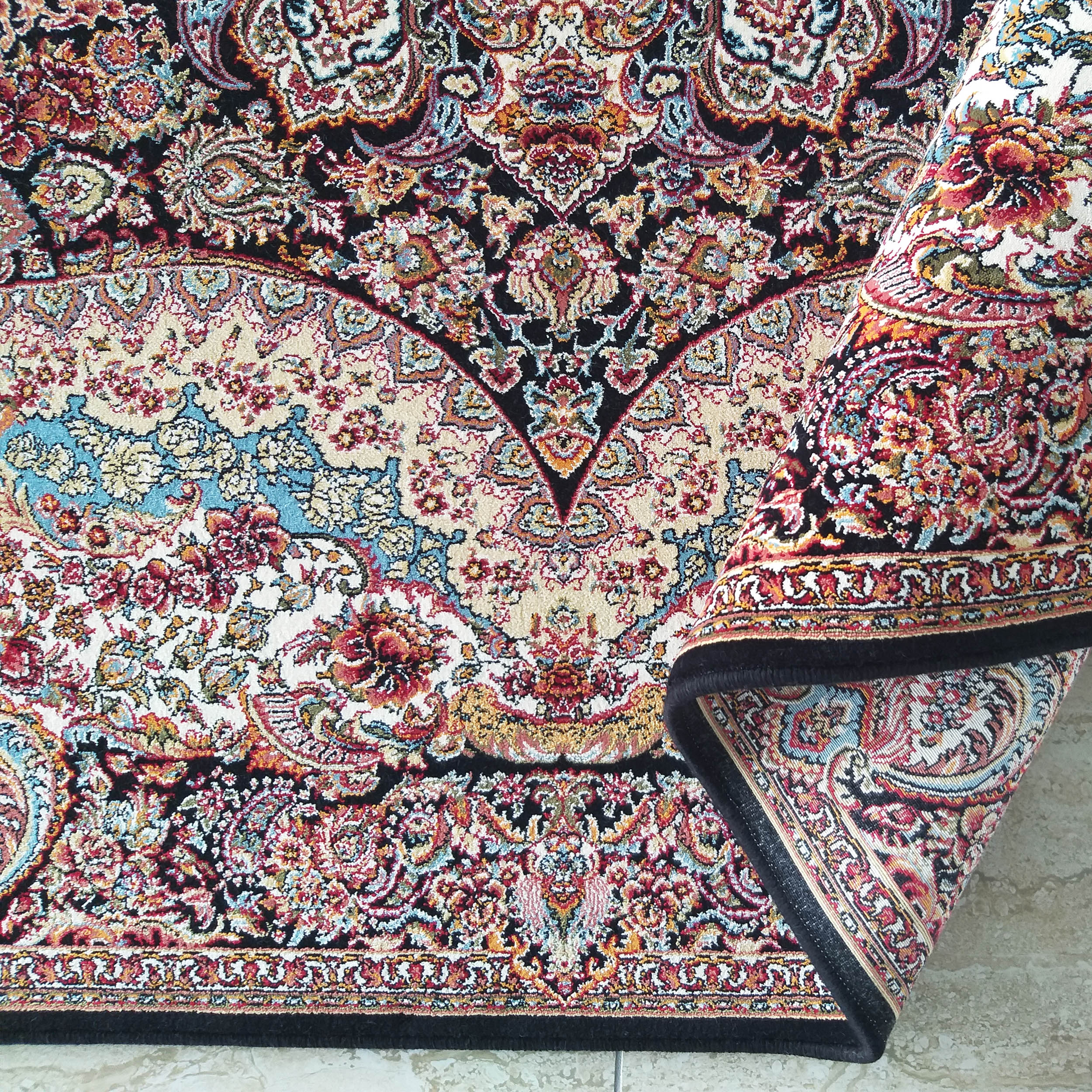 Tapis à motifs floraux et cachemire complexes, rouge, or, bleu et crème sur fond noir, partiellement roulé sur un sol clair