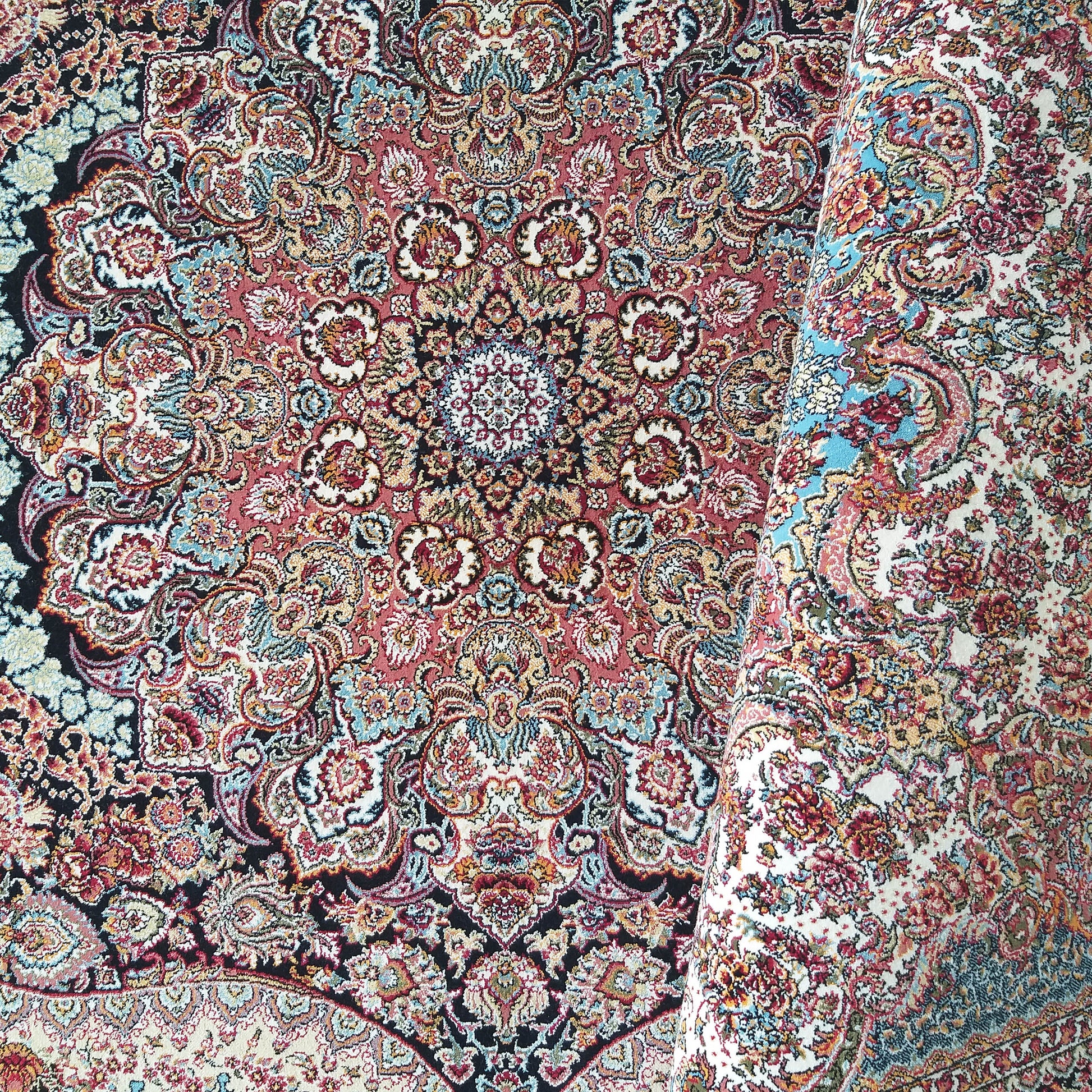 Tapis enroulé aux motifs floraux et arabesques complexes, médaillon central, dominant rouge, noir, crème, bleu et or