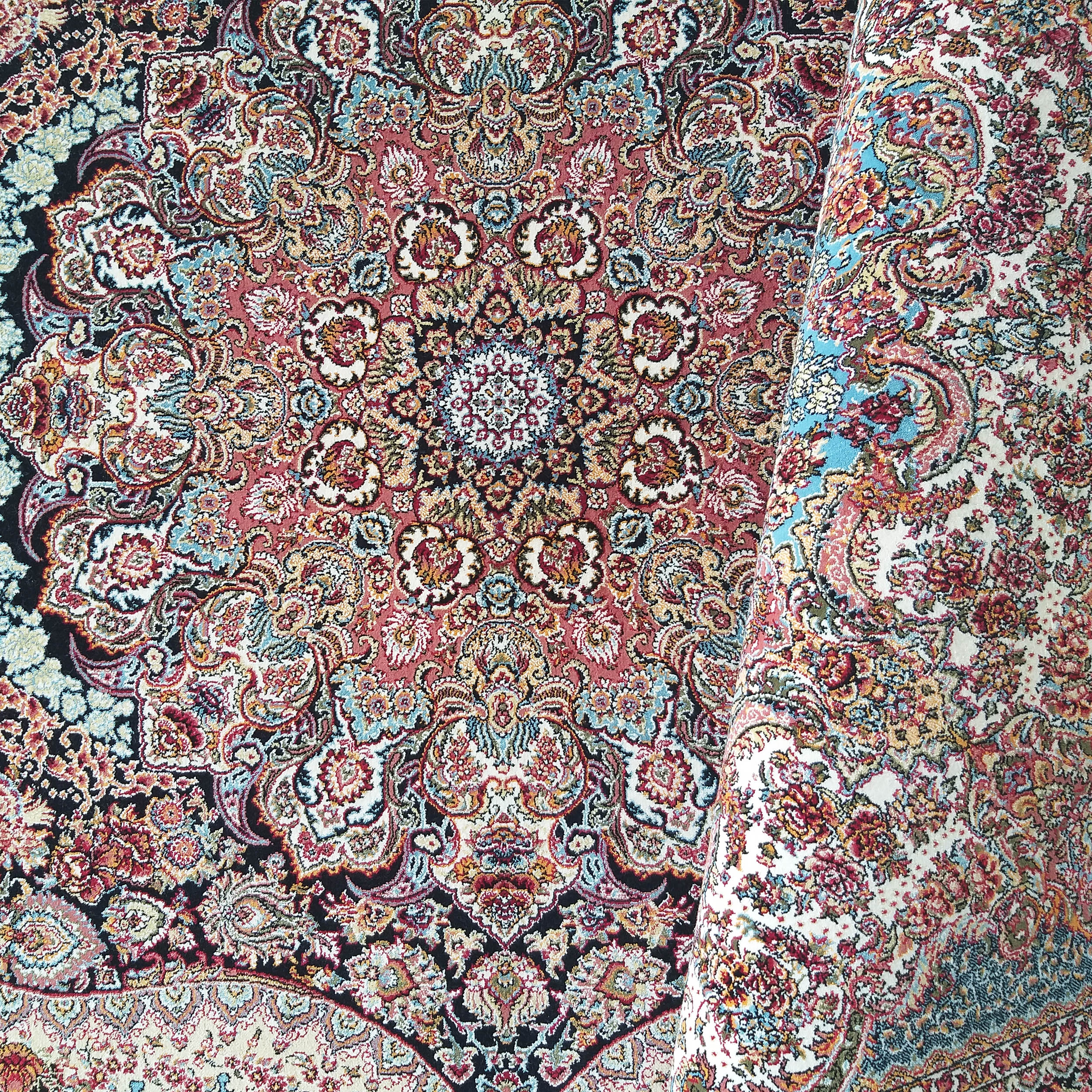 Tapis enroulé aux motifs floraux et arabesques complexes, médaillon central, dominant rouge, noir, crème, bleu et or