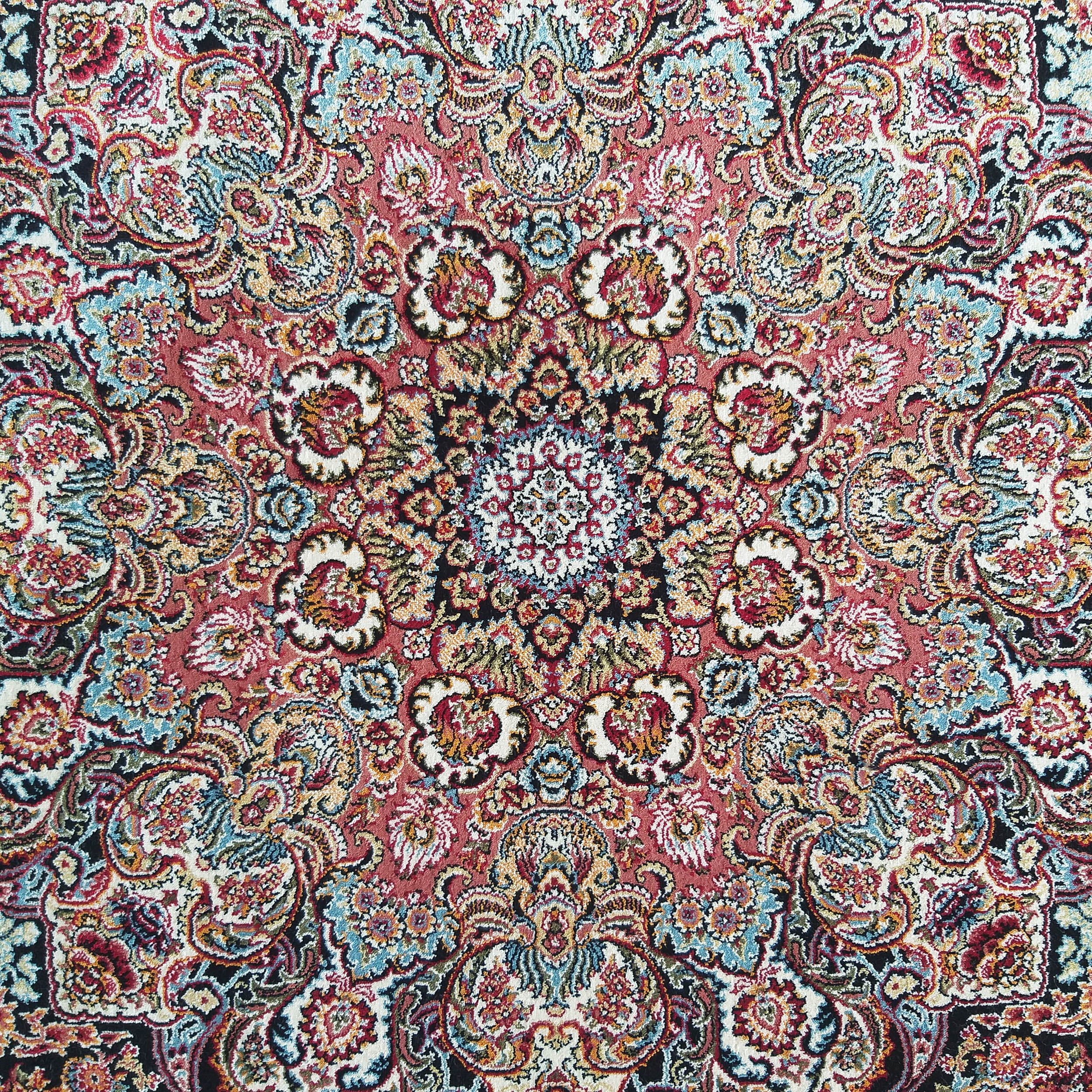 Gros plan sur un tapis orné de motifs floraux et cachemire symétriques, aux couleurs rose, bleu, or, blanc et noir