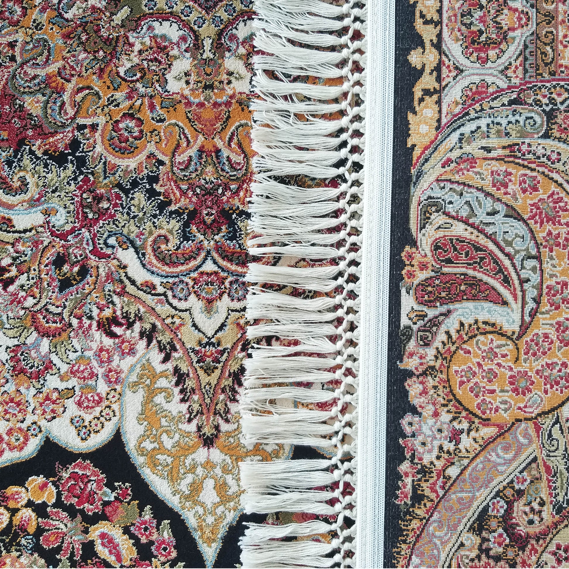 Tapis orné de motifs floraux et cachemire multicolores, avec des franges blanches. Couleurs principales: rouge, or, noir