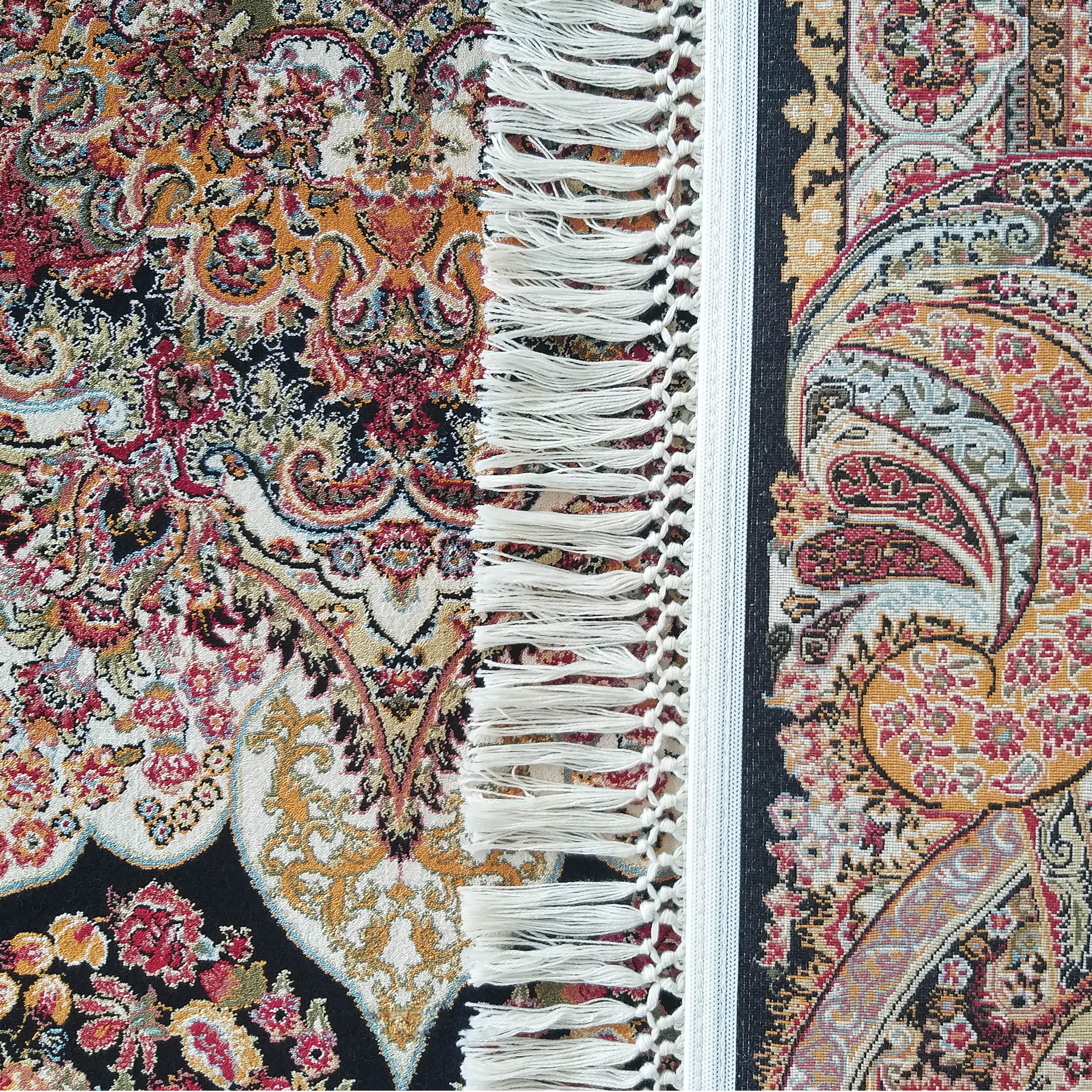 Tapis orné de motifs floraux et cachemire multicolores, avec des franges blanches. Couleurs principales: rouge, or, noir