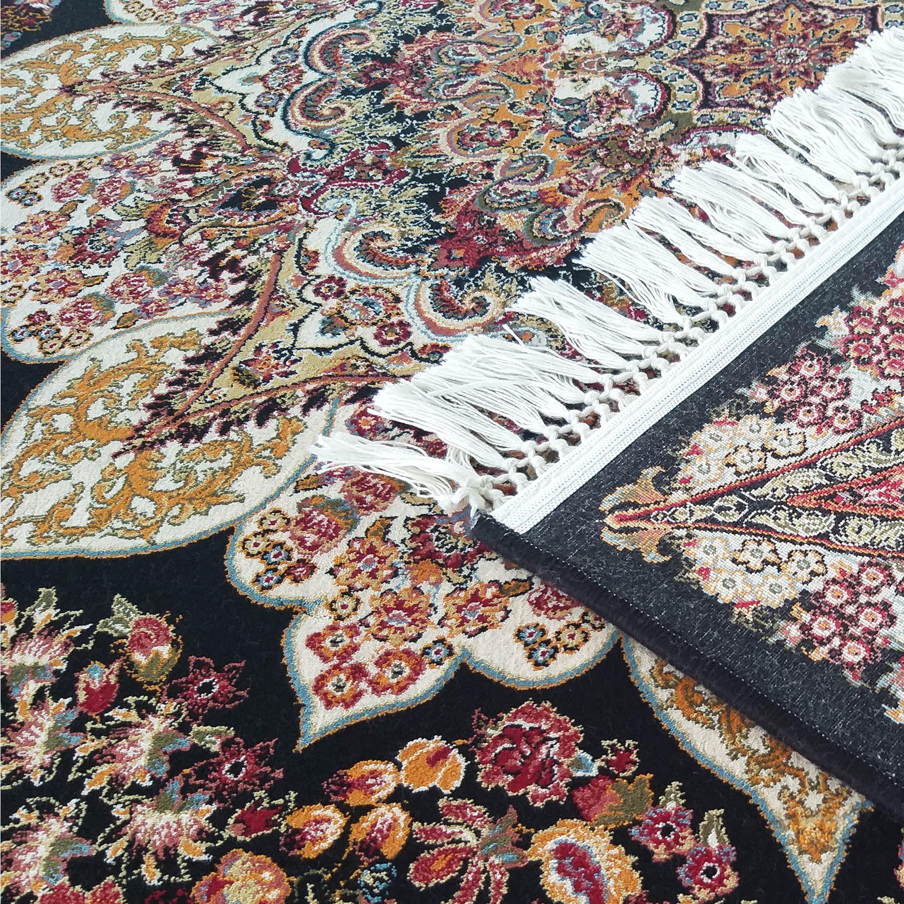 Tapis aux motifs floraux persans complexes sur fond noir, aux couleurs rouge, or, crème et bleu, avec des franges blanches