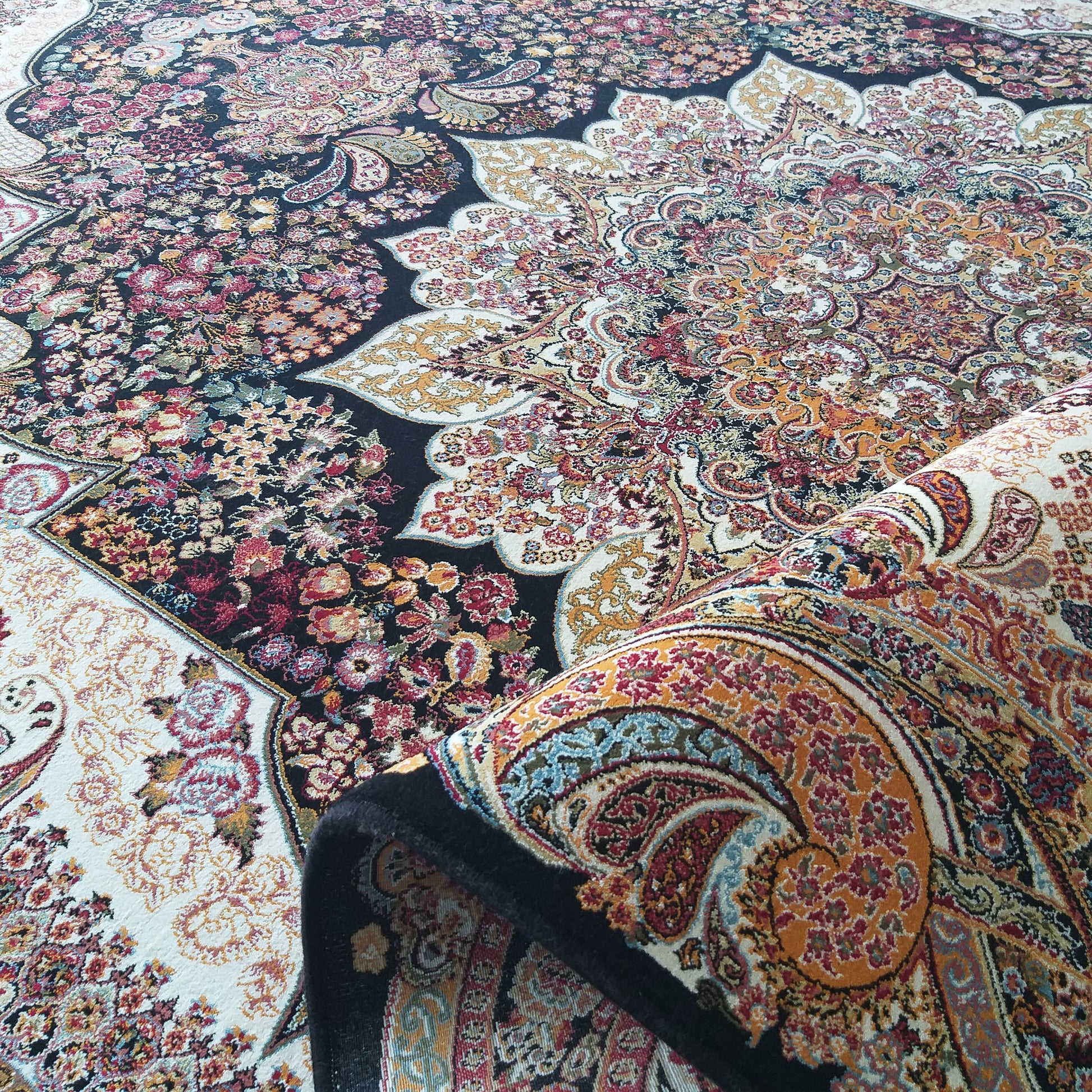 Tapis à motifs floraux et cachemire complexes, richement coloré en noir, crème, rouge, or et bleu, dont une partie est roulée