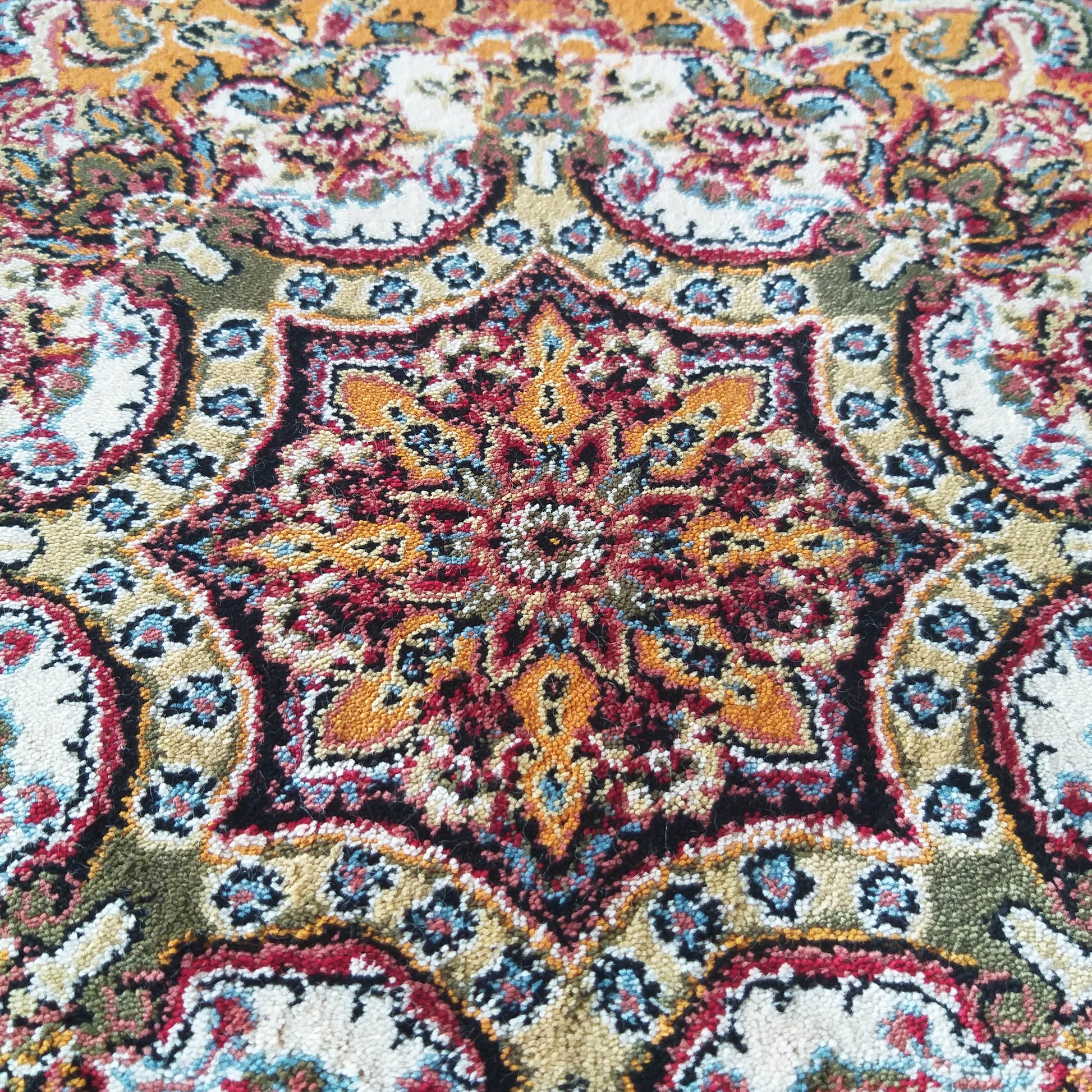 Tapis aux motifs ornementaux. Étoile centrale rouge, or et noire sur fond crème, détails floraux bleus et verts