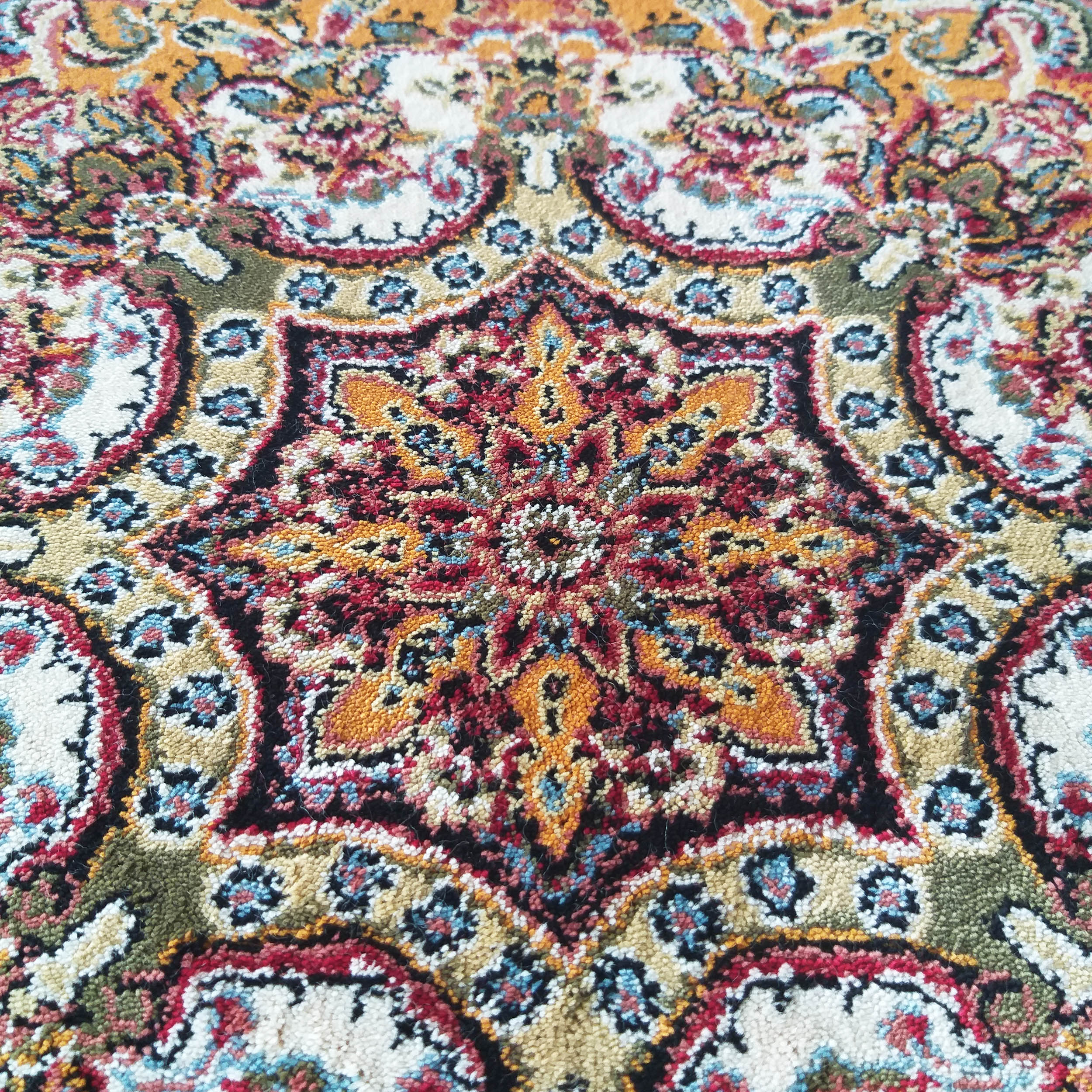 Tapis aux motifs ornementaux. Étoile centrale rouge, or et noire sur fond crème, détails floraux bleus et verts