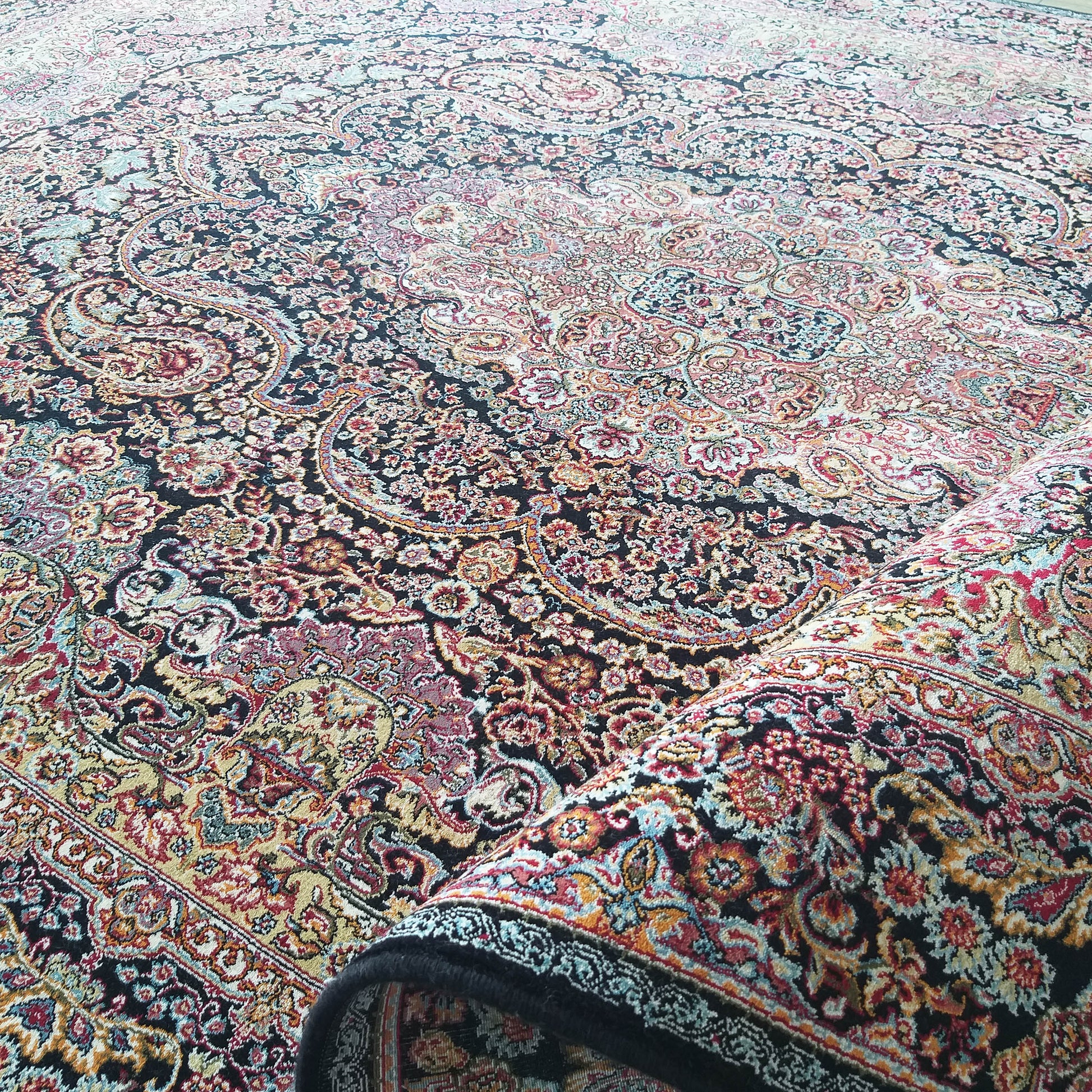 Tapis à motifs floraux et cachemire riches et détaillés, dominé par le noir, rouge, or, bleu et crème, partiellement enroulé