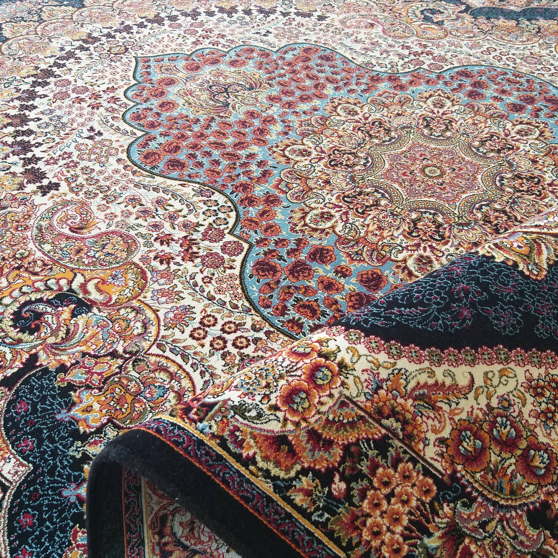 Tapis richement décoré de motifs floraux et cachemire multicolores sur fond crème, légèrement enroulé