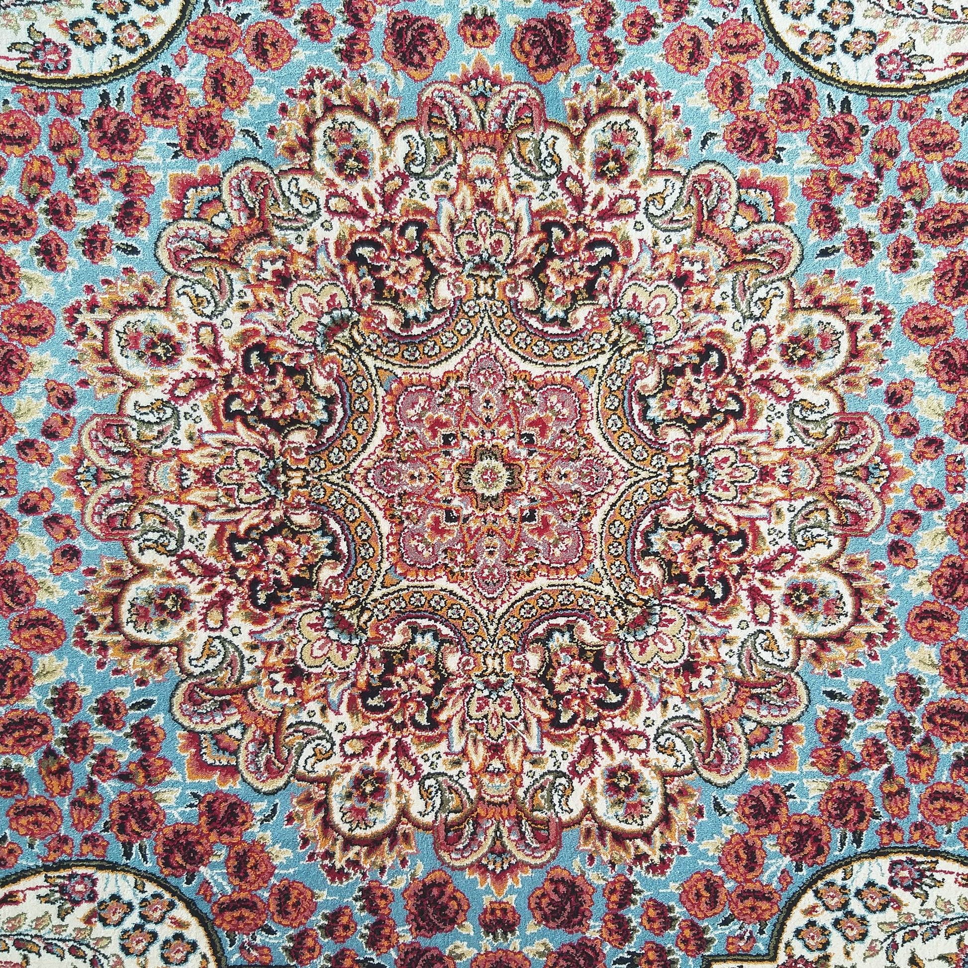 Tapis floral orné. Le tapis affiche un grand médaillon central rouge, crème et orange sur un fond bleu clair parsemé de roses