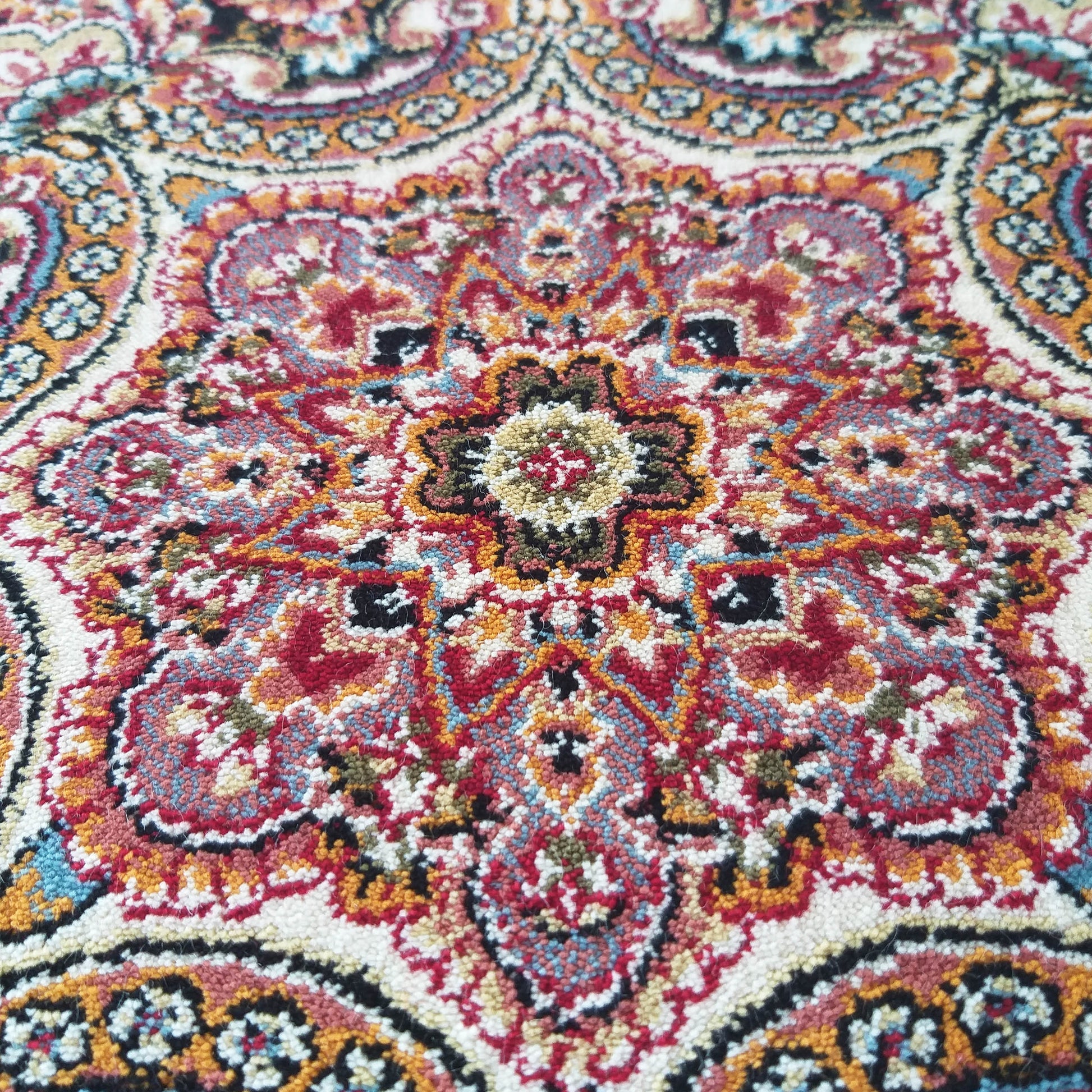Gros plan sur un tapis aux motifs orientaux complexes. Les couleurs vives dominantes sont le rouge, l'orange, le crème et le bleu turquoise