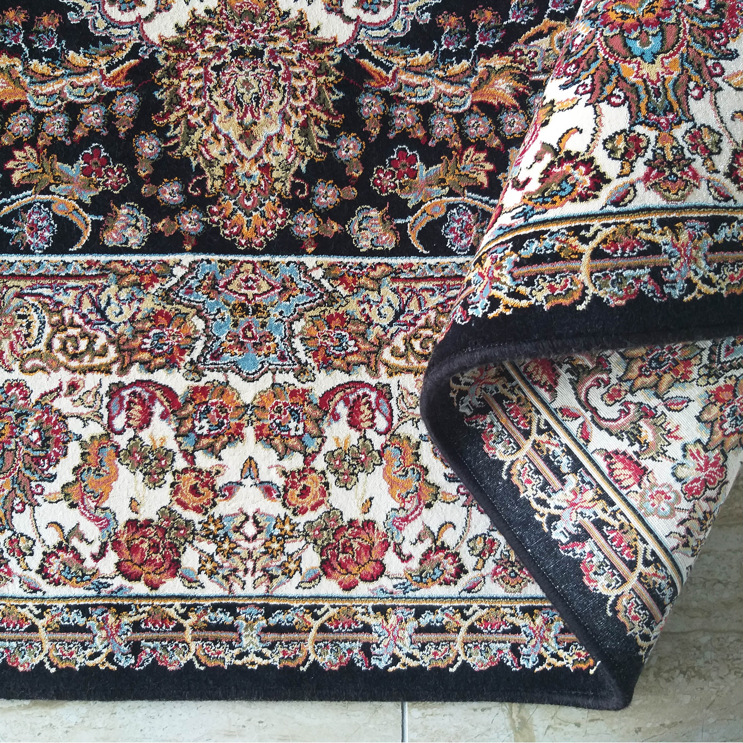 Tapis textile avec motifs floraux complexes aux couleurs vives sur fonds noir et crème, partiellement roulé