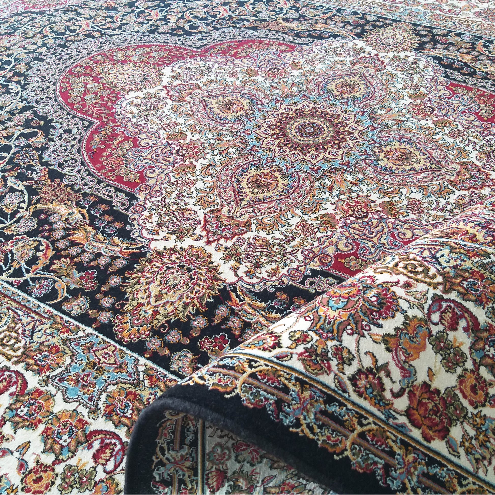 Tapis à motifs floraux et arabesques détaillés, médaillon central, en noir, crème, rouge et or. Le tapis est partiellement roulé