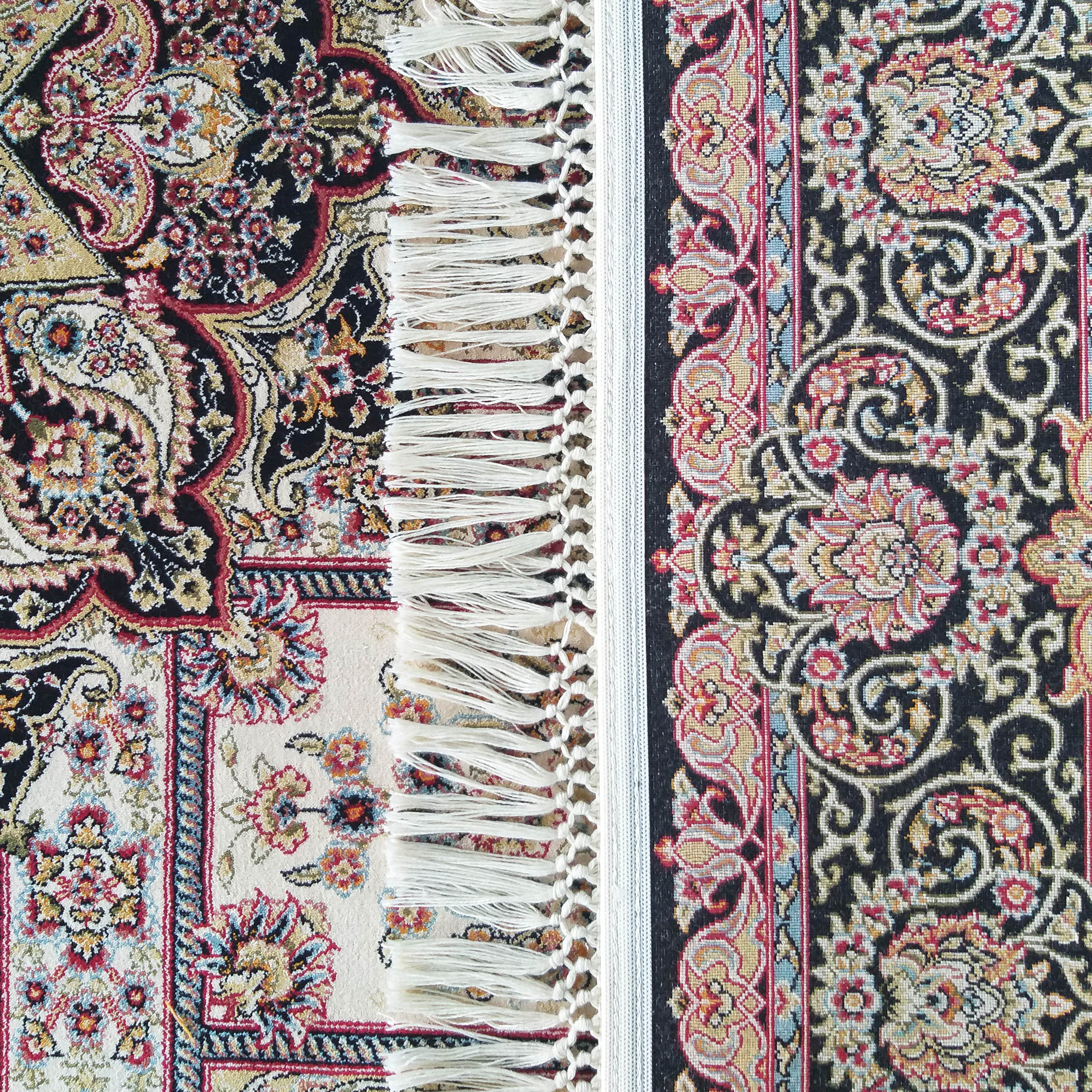 Gros plan d'un tapis à motifs floraux et cachemire sur fond noir et crème, aux détails rouges, or et bleus, avec franges