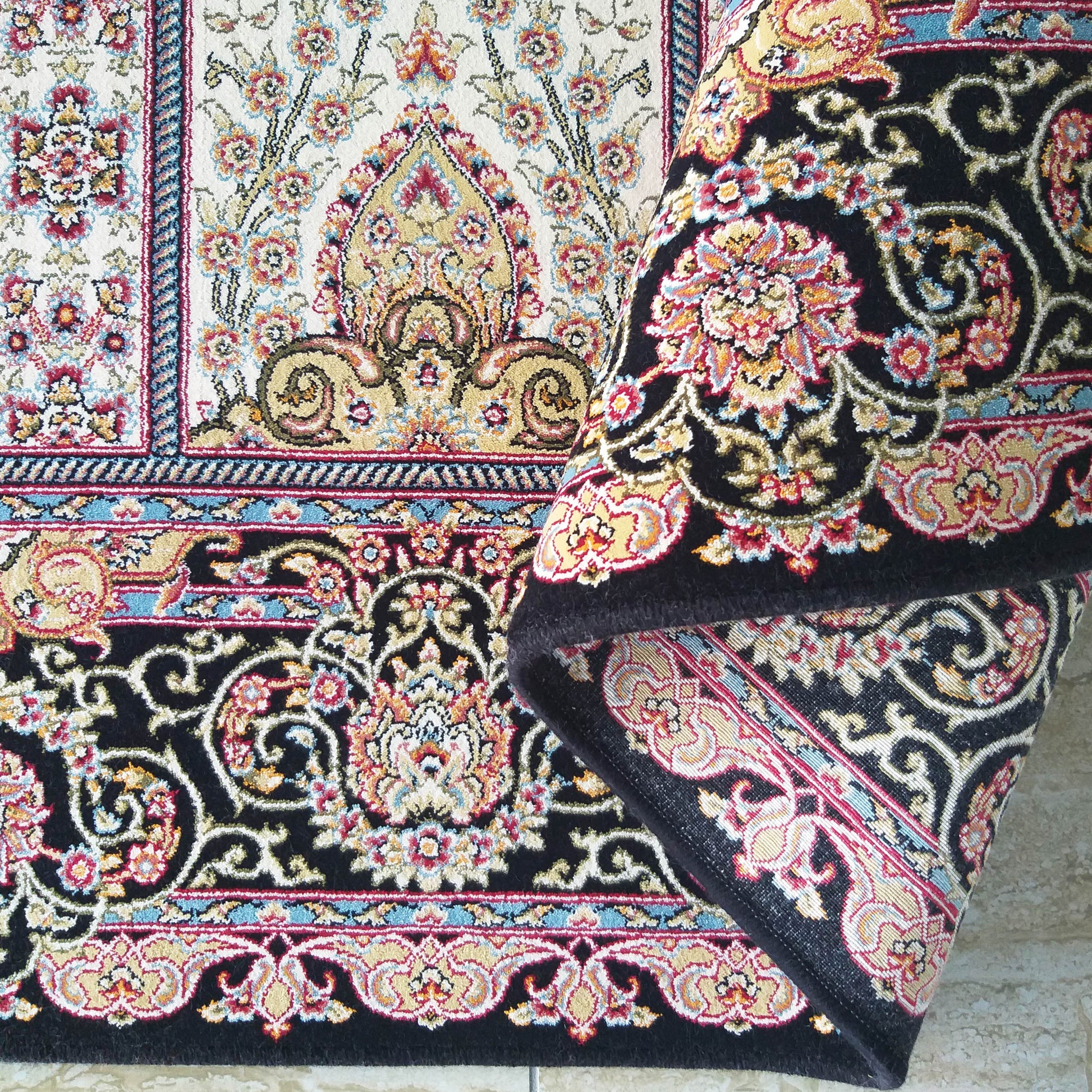 Tapis aux motifs floraux et arabesques traditionnels en crème, noir, rouge, bleu et or. Une partie du tapis est enroulée