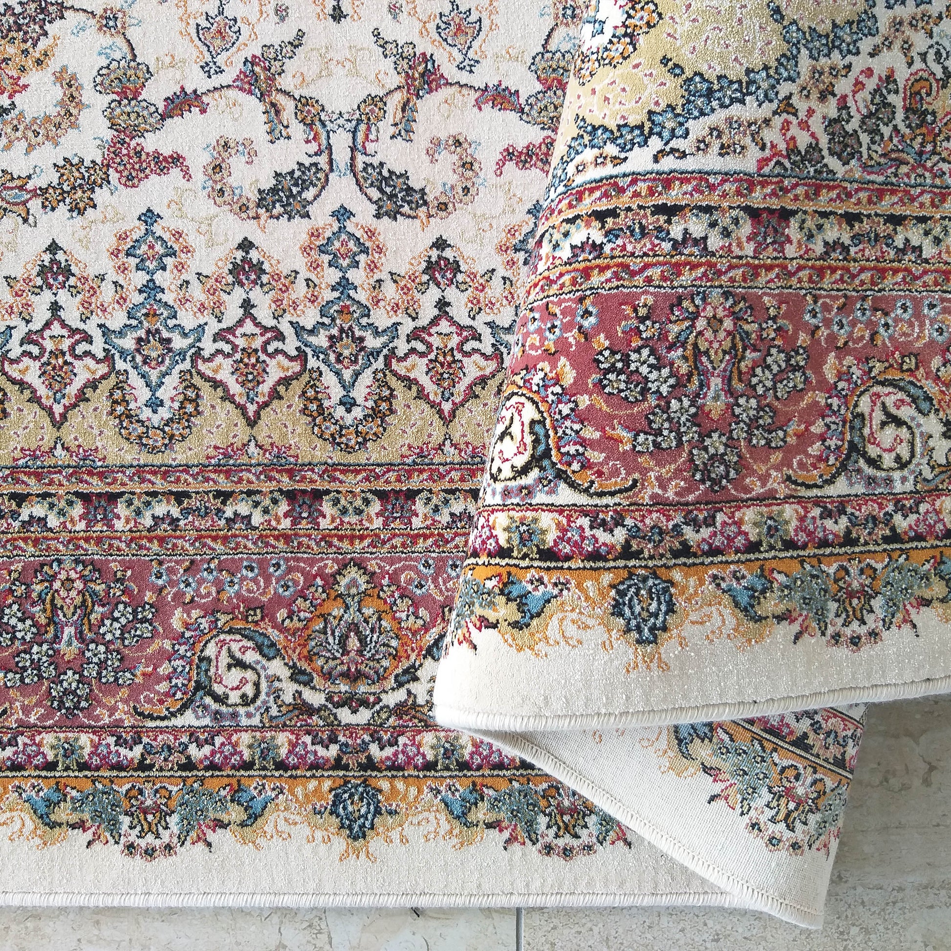 Tapis crème aux motifs traditionnels riches en rouge, bleu, or, noir et vert, avec des bordures détaillées et une partie enroulée