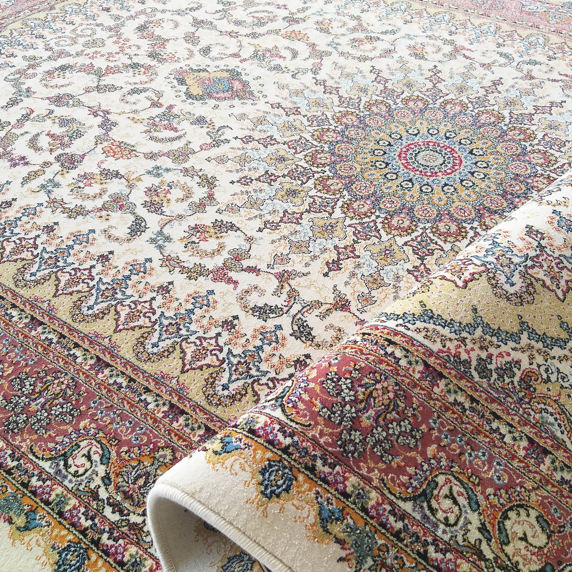 Tapis crème à motifs floraux ornementaux et un médaillon central richement colorés, partiellement roulé