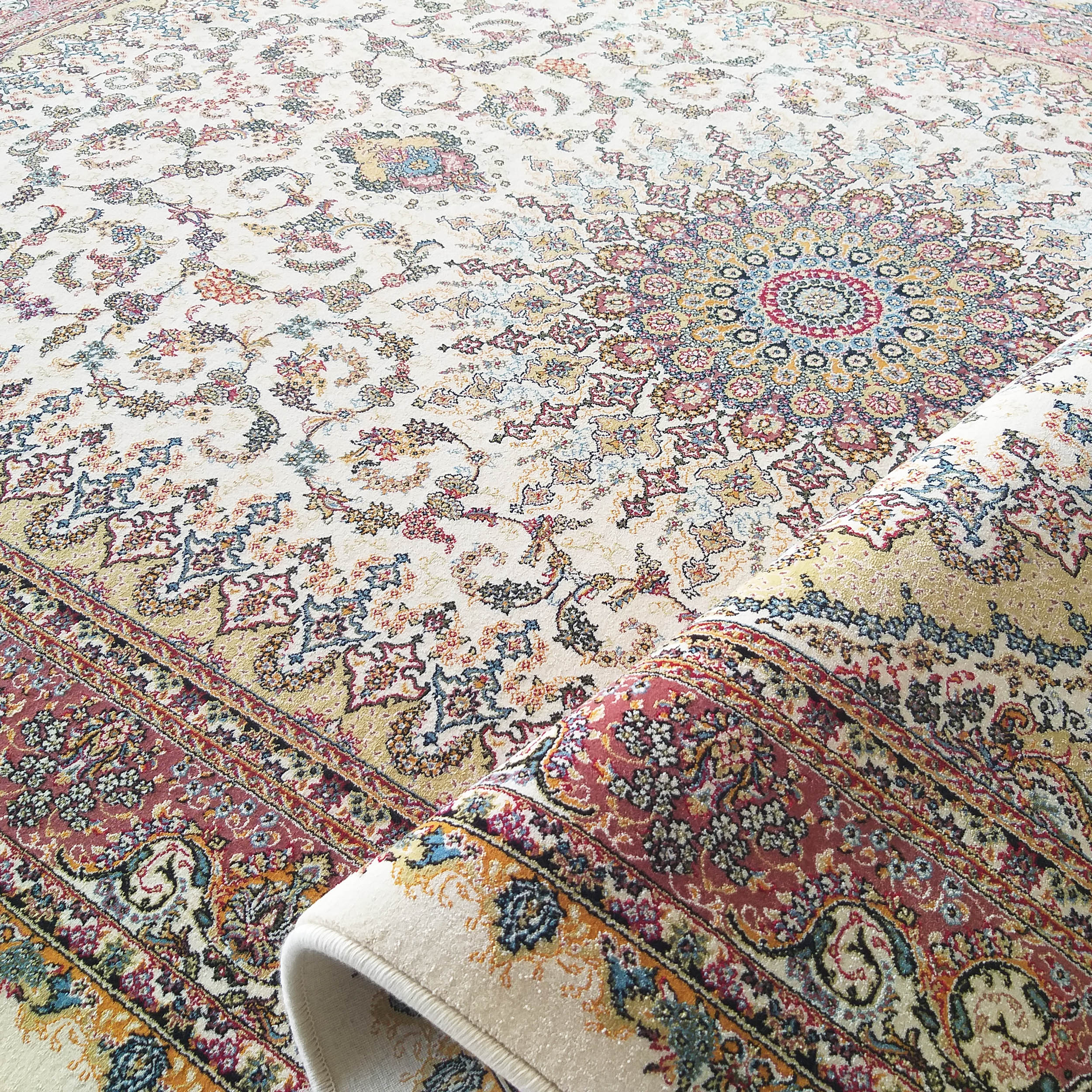 Tapis crème à motifs floraux ornementaux et un médaillon central richement colorés, partiellement roulé
