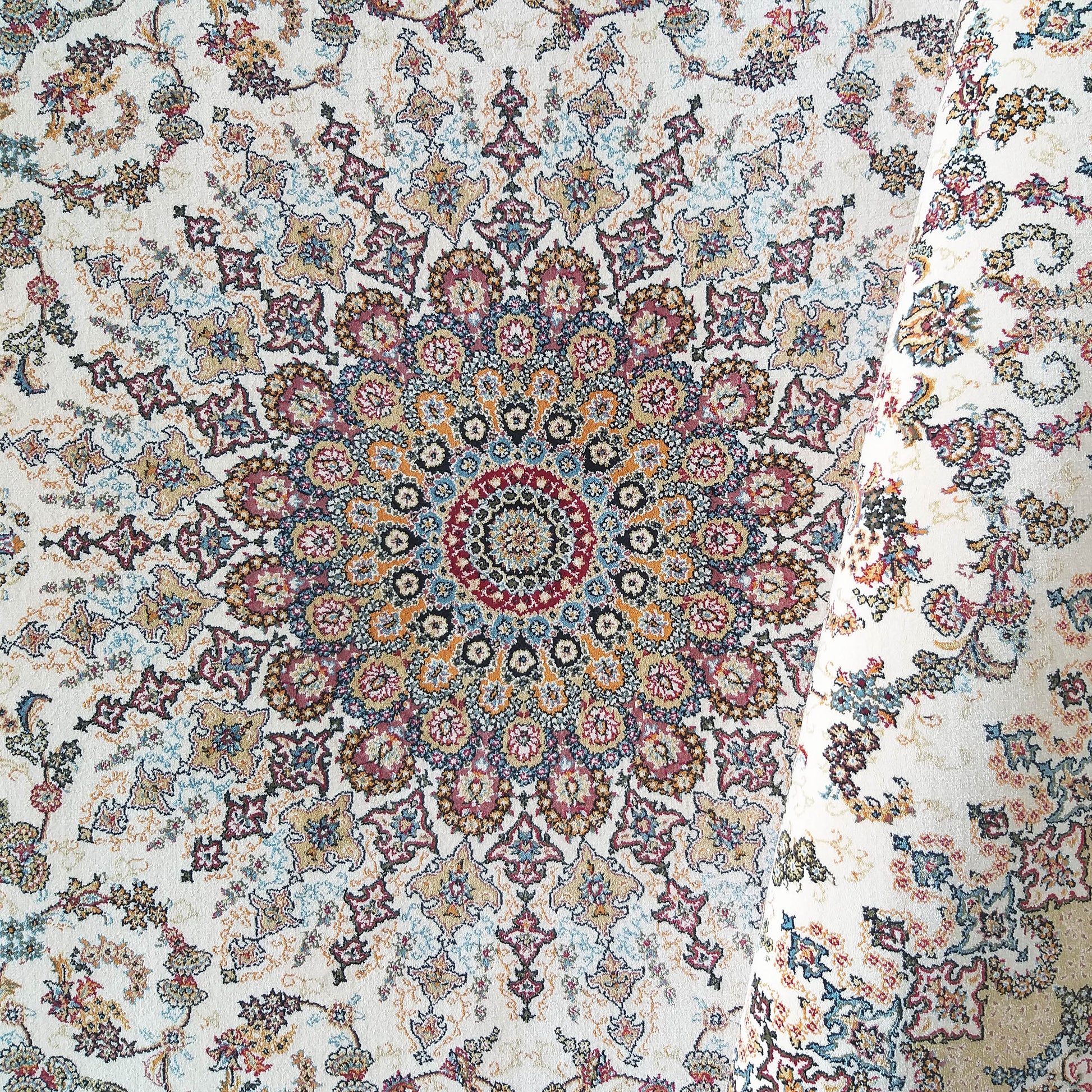 Tapis crème à motifs traditionnels, avec un grand médaillon central richement détaillé en rouge, bleu et or, une partie enroulée