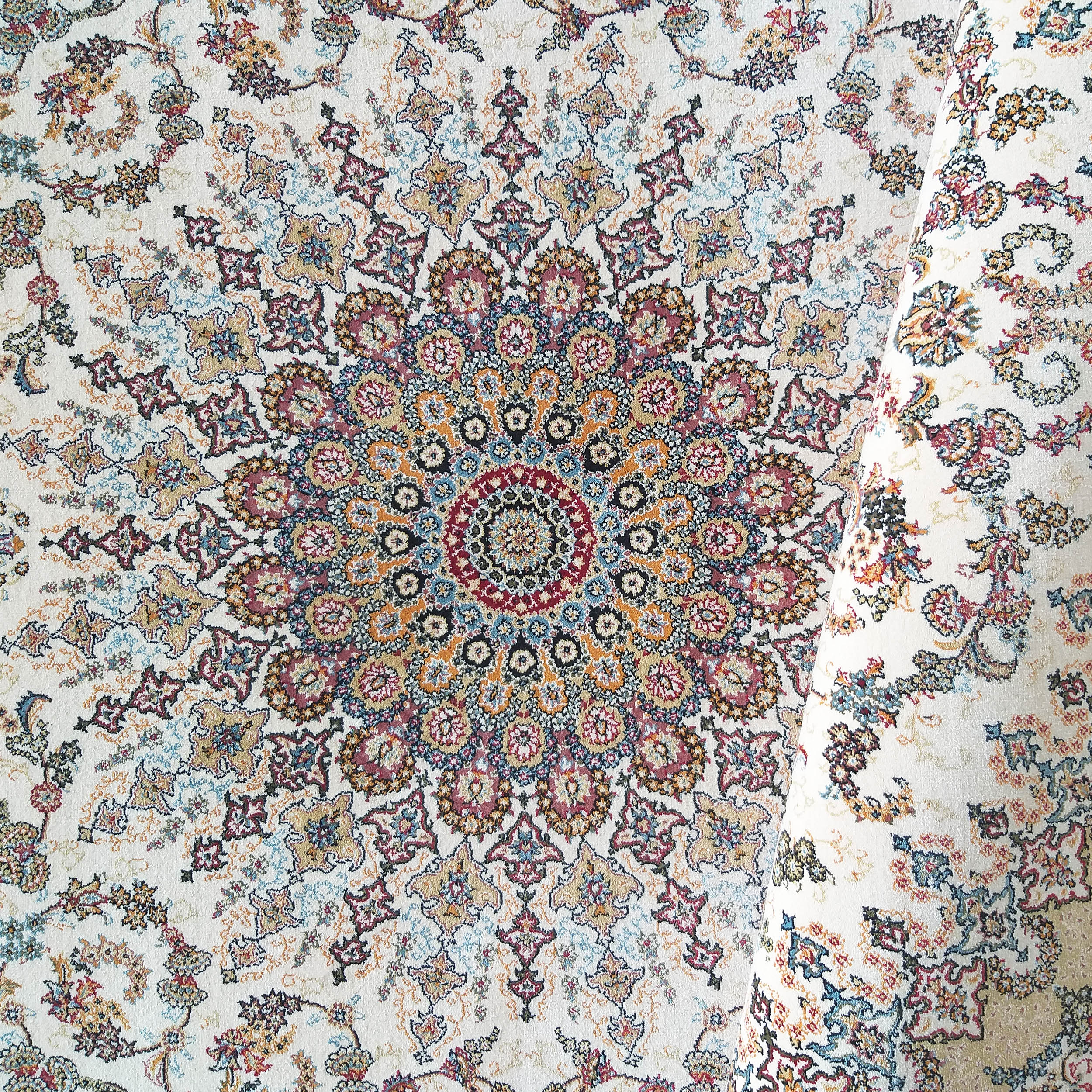 Tapis crème à motifs traditionnels, avec un grand médaillon central richement détaillé en rouge, bleu et or, une partie enroulée