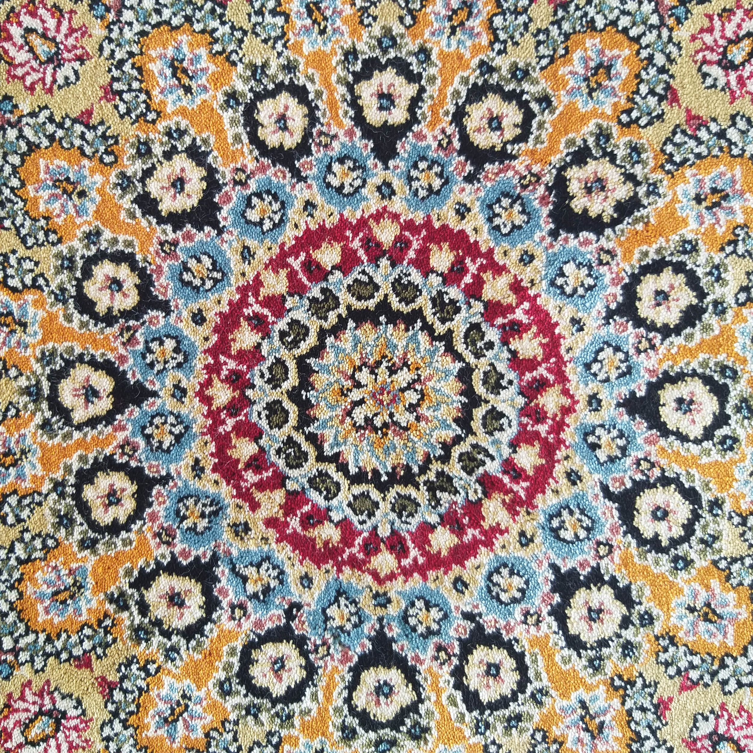 Tapis à motif central ornemental, aux couleurs vives : rouge, or, orange, bleu et noir sur fond clair, avec texture textile détaillée