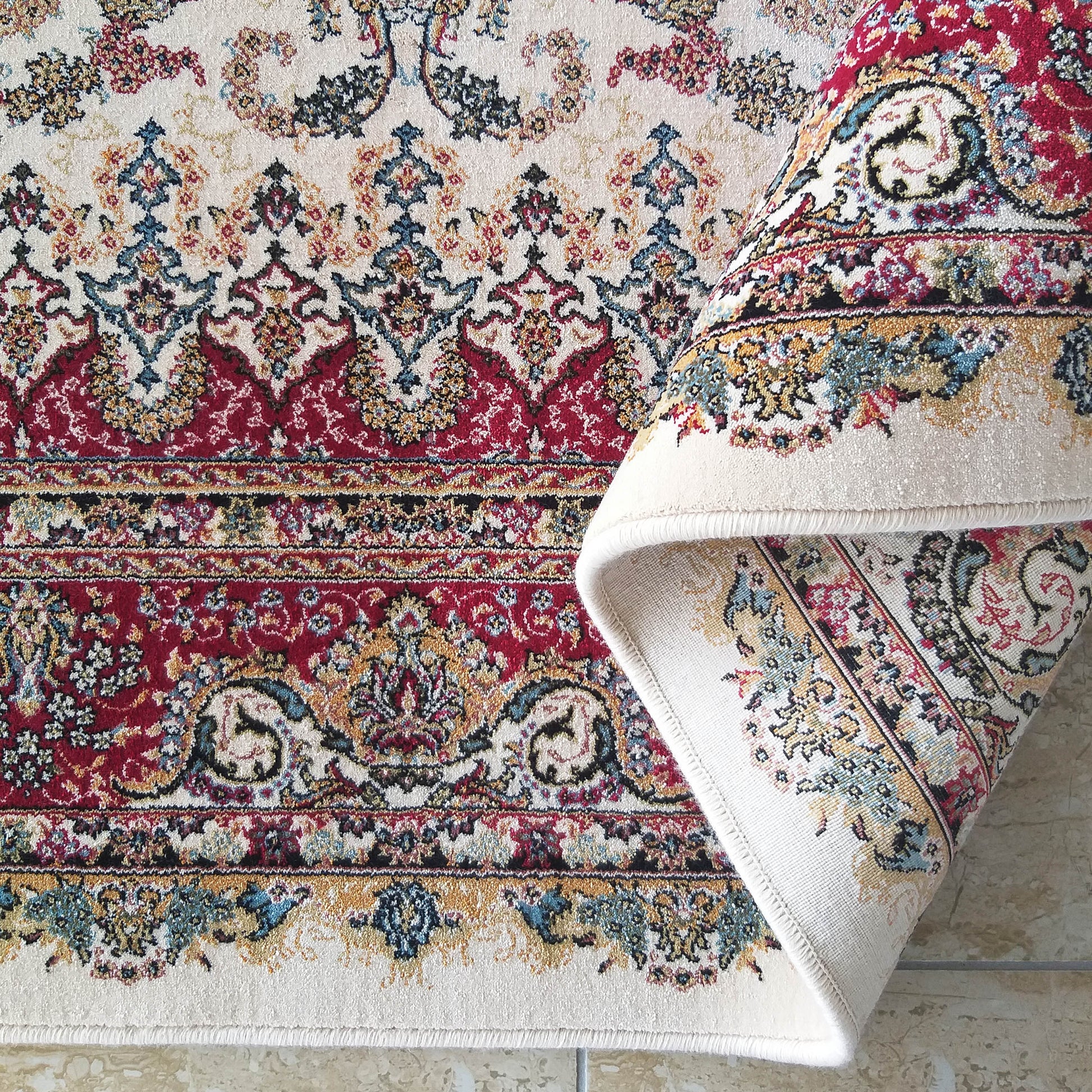 Tapis épais à motifs floraux détaillés crème, rouge bordeaux, bleu et doré, partiellement enroulé