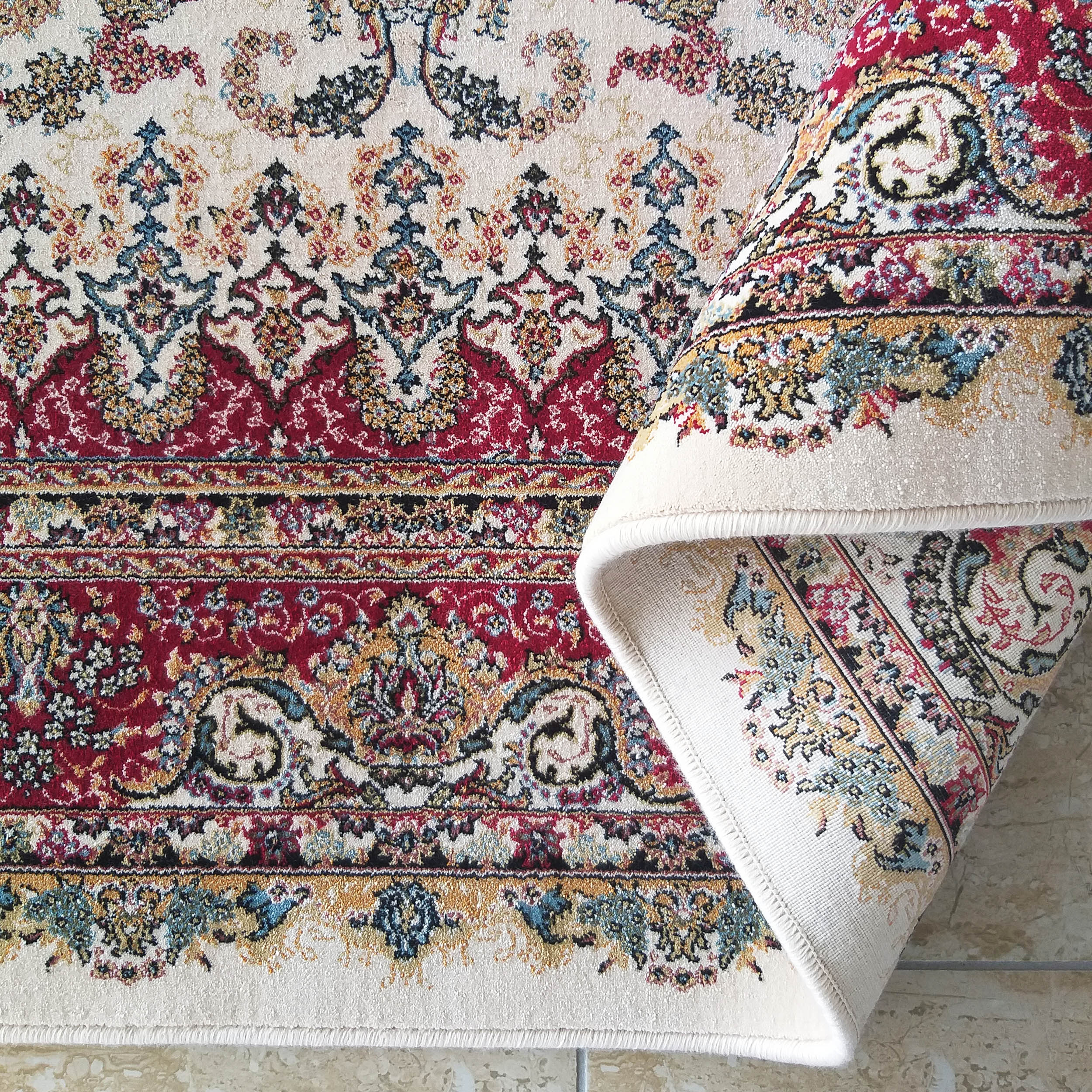 Tapis épais à motifs floraux détaillés crème, rouge bordeaux, bleu et doré, partiellement enroulé