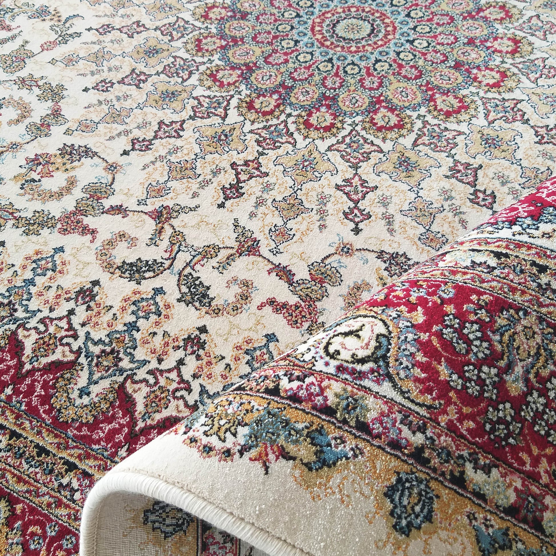 Tapis à motifs ornementaux traditionnels enroulé, aux couleurs crème, rouge, bleu et or