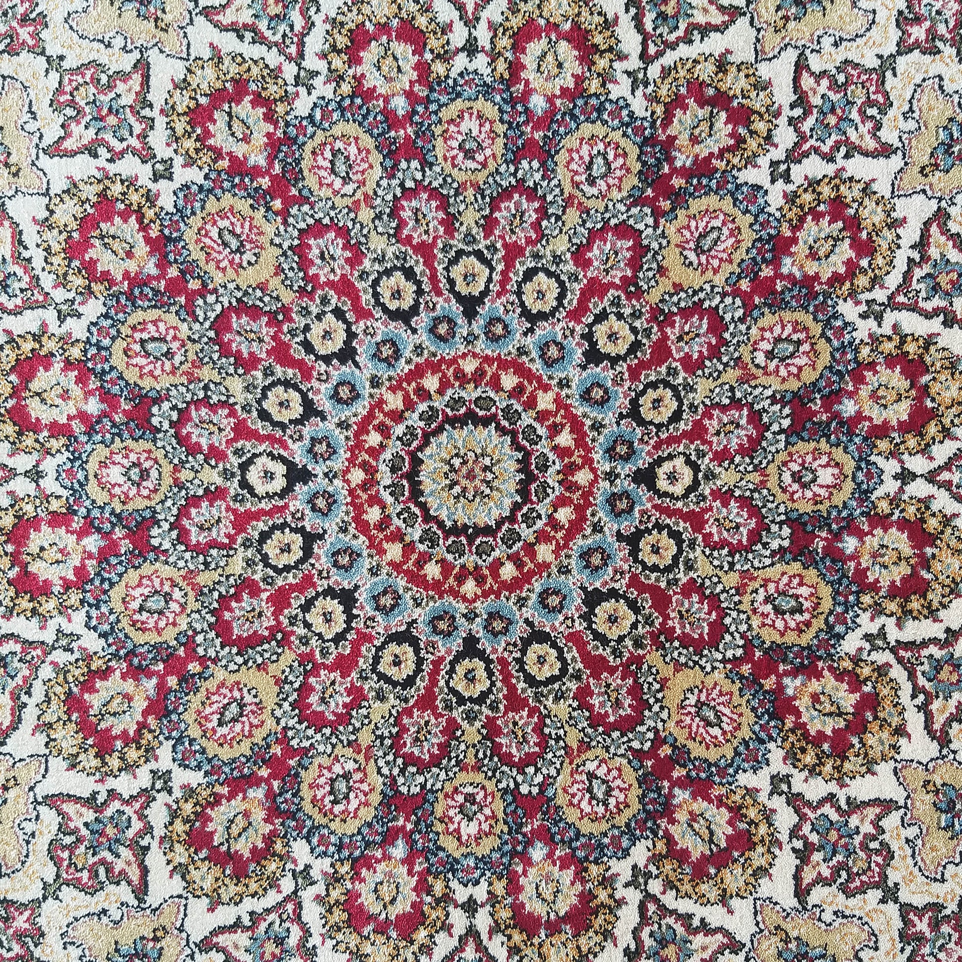 Tapis aux motifs floraux et ornementaux, centré sur un grand médaillon. Les couleurs vives incluent le rouge, le crème, le doré et le bleu