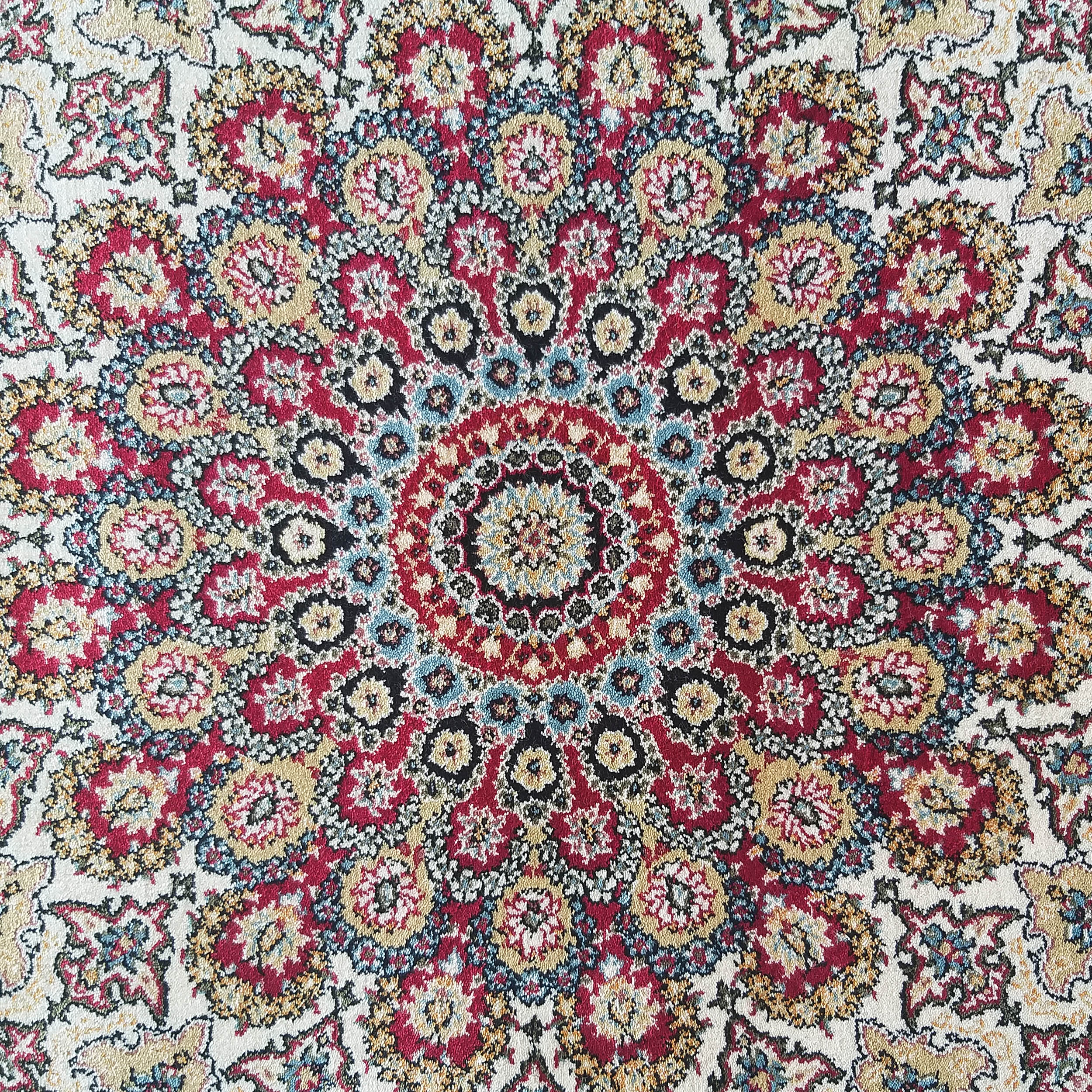 Tapis aux motifs floraux et ornementaux, centré sur un grand médaillon. Les couleurs vives incluent le rouge, le crème, le doré et le bleu