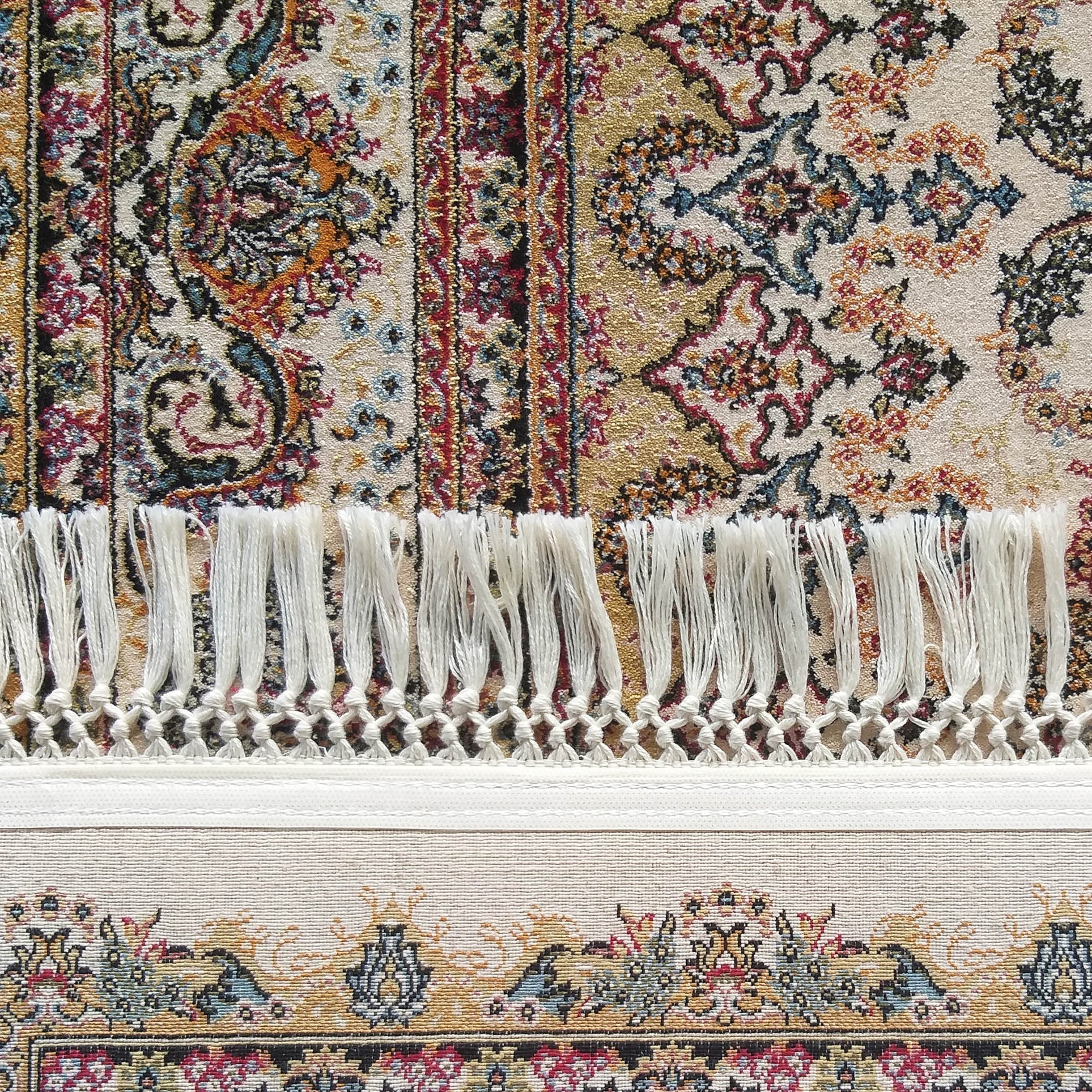 Tapis aux motifs floraux et cachemire en rouge, or, bleu et vert sur un fond crème, bordé d'une frange claire