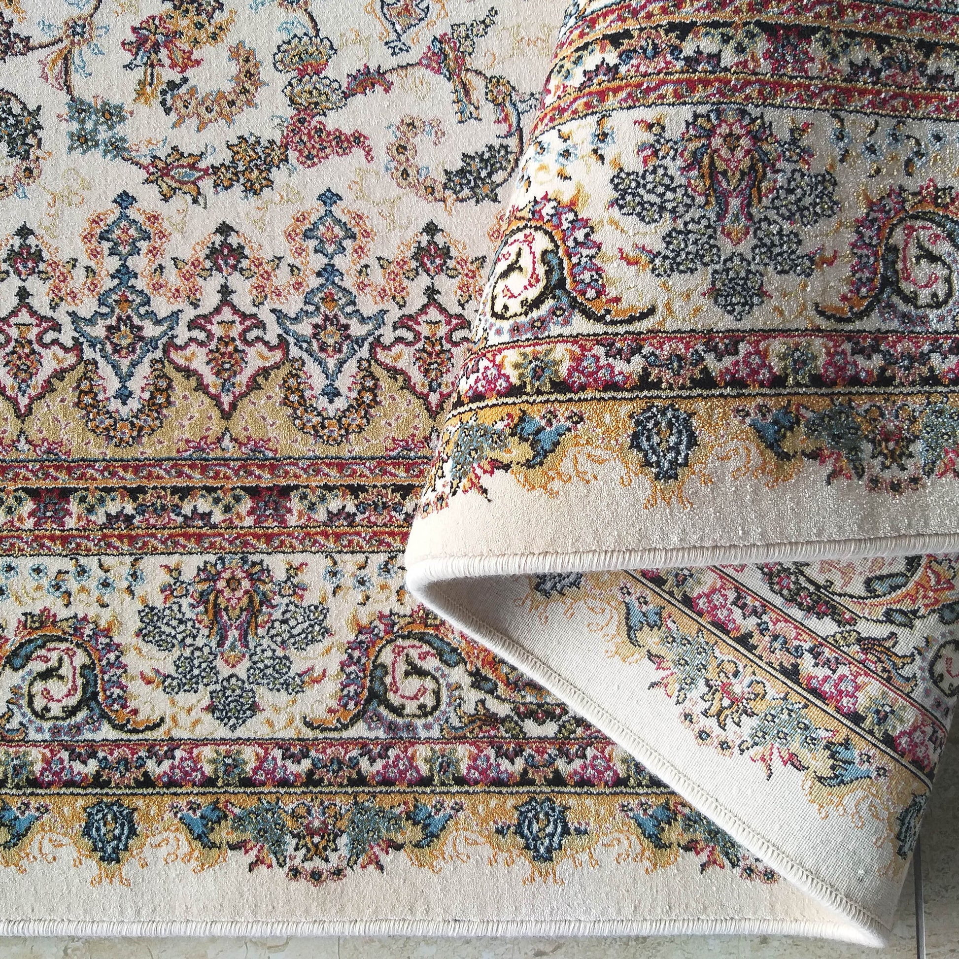 Tapis ivoire à motifs floraux et ornementaux colorés en rouge, bleu, jaune et noir, une section est roulée