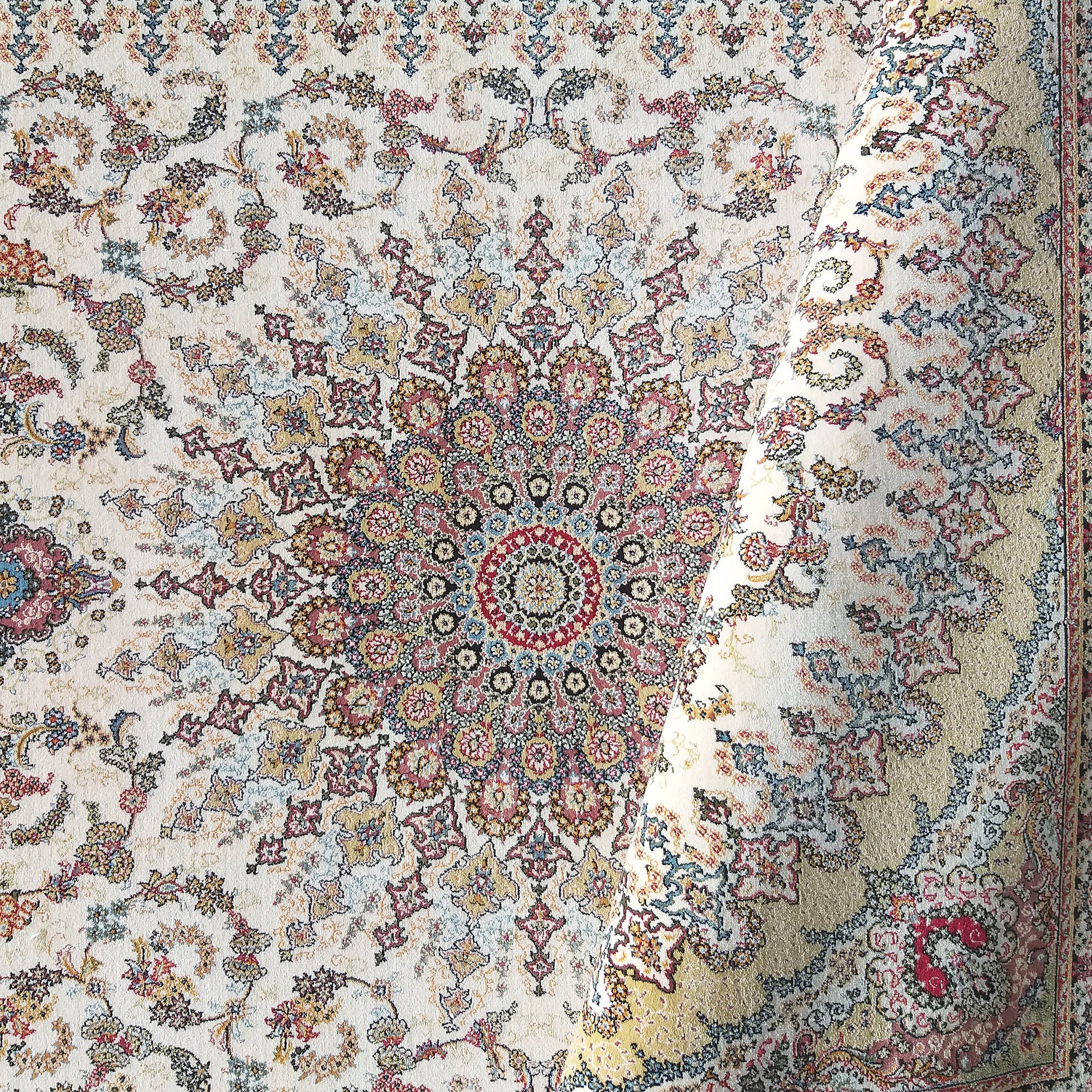Tapis à fond crème orné de motifs floraux multicolores et d'un grand médaillon central, avec une section enroulée