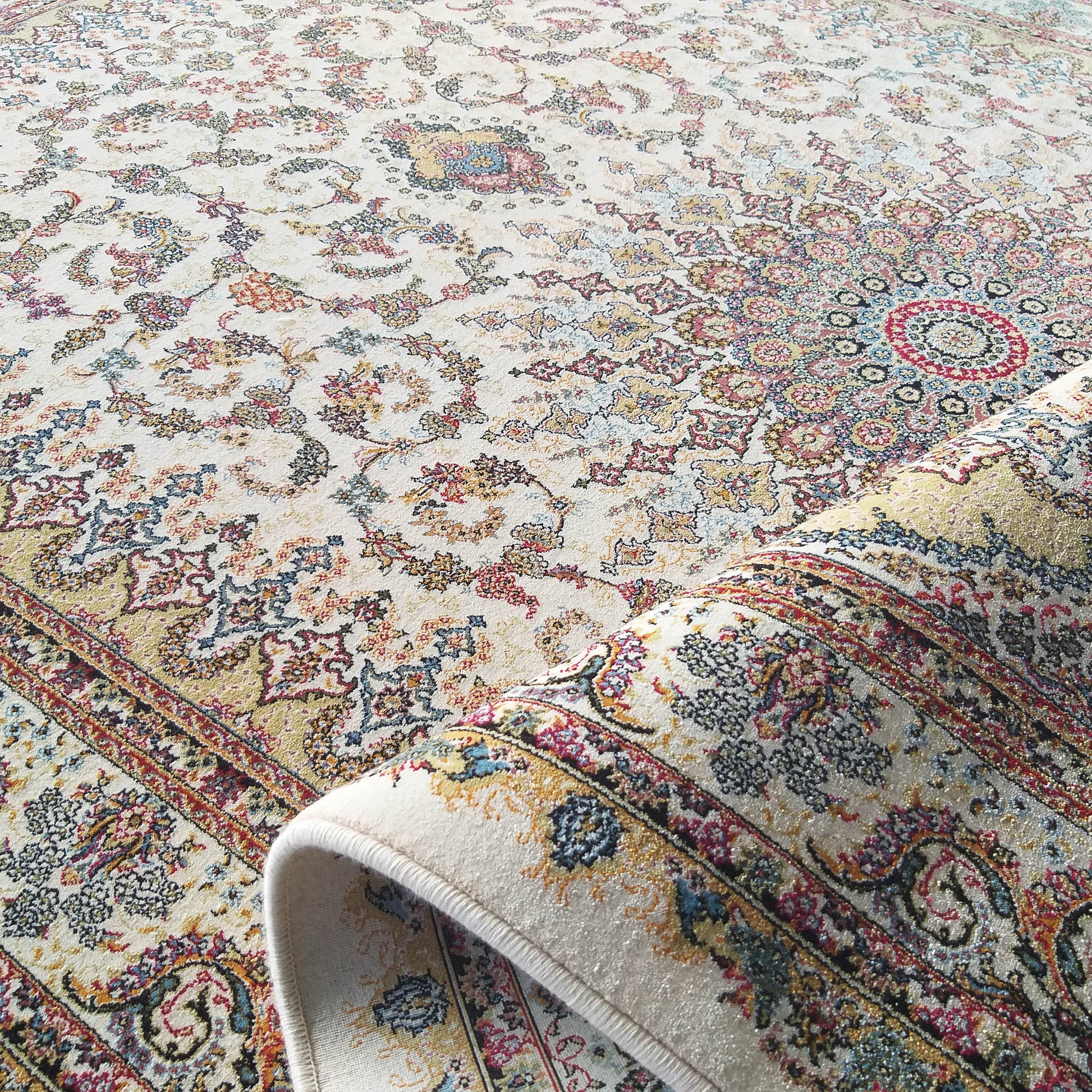 Tapis à fond crème, richement décoré de motifs floraux ornementaux multicolores rouges, bleus, dorés, partiellement roulé