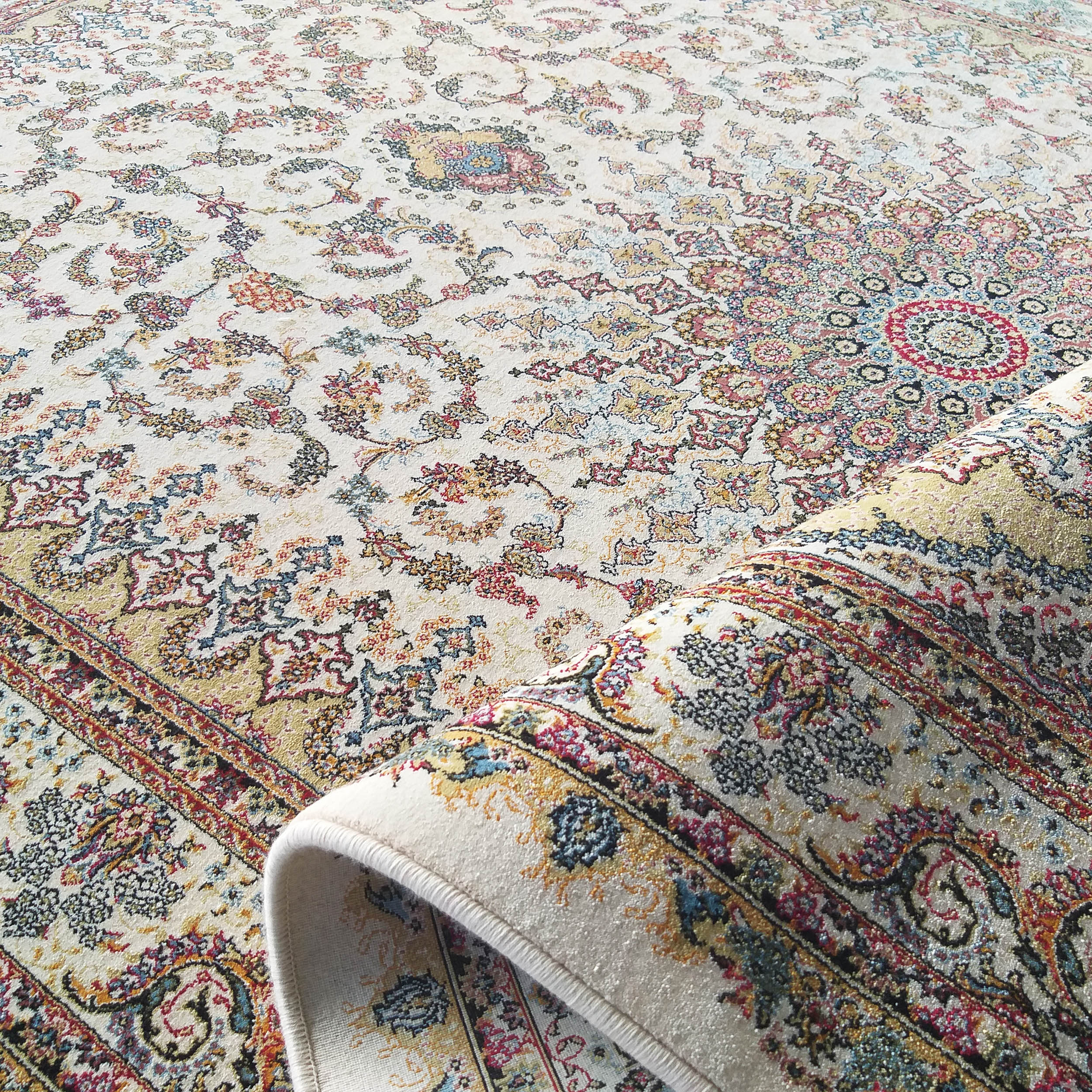 Tapis à fond crème, richement décoré de motifs floraux ornementaux multicolores rouges, bleus, dorés, partiellement roulé
