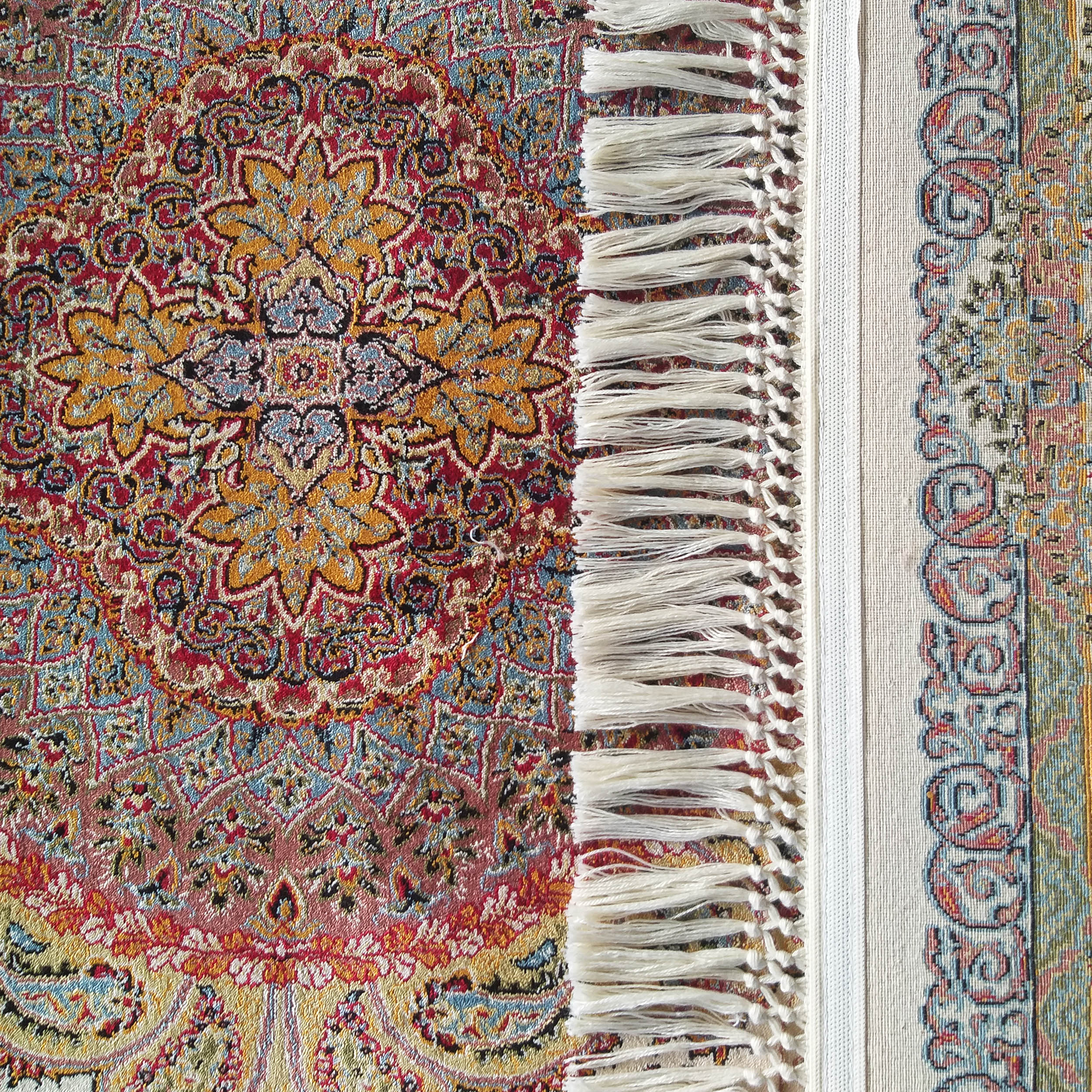 Tapis coloré aux riches motifs floraux orientaux rouges, or et bleus, avec des franges blanches et une bordure ornée plus claire
