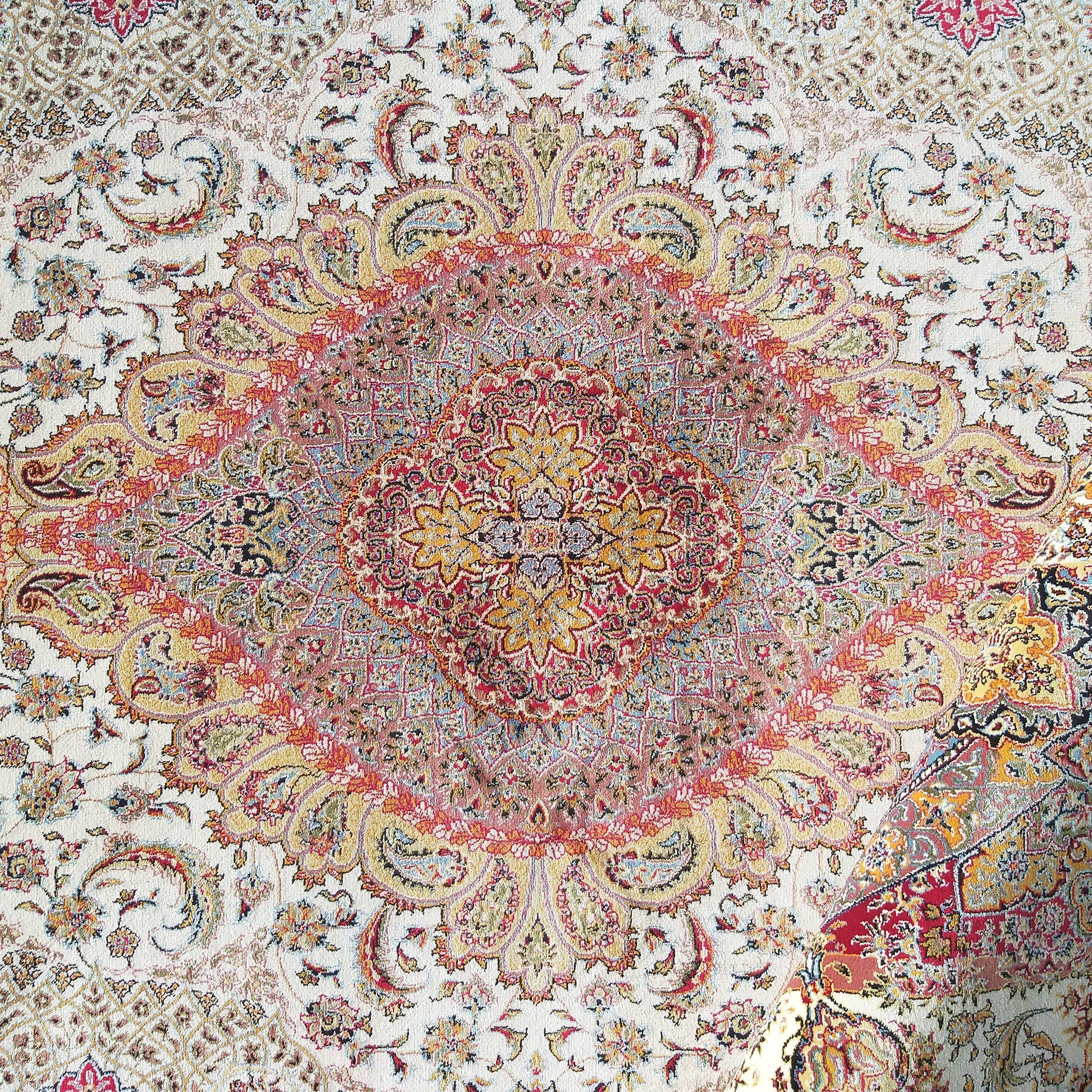 Tapis à motifs floraux et arabesques complexes avec un grand médaillon central. Fond crème dominé par du rouge, jaune et bleu