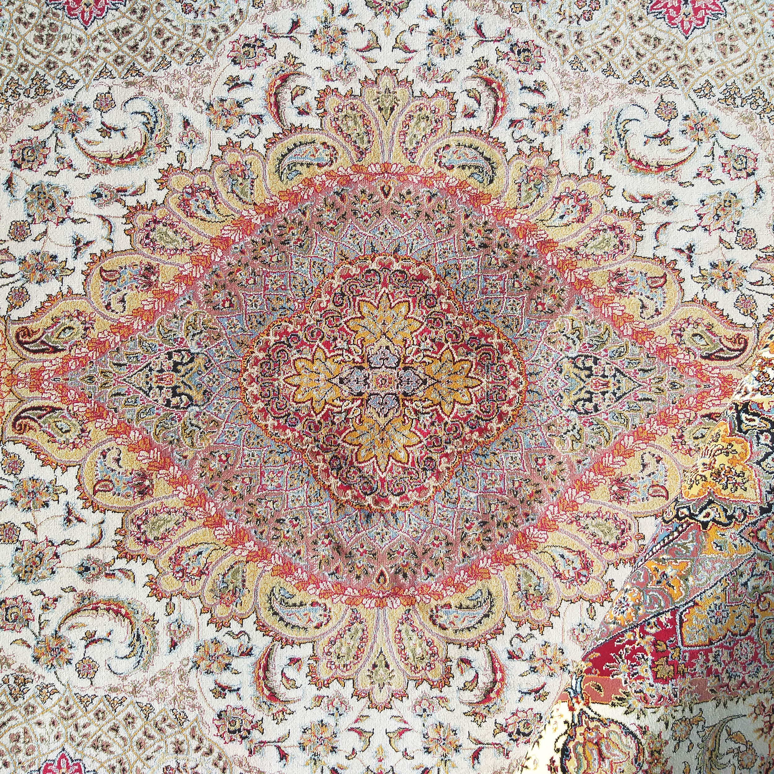 Tapis à motifs floraux et arabesques complexes avec un grand médaillon central. Fond crème dominé par du rouge, jaune et bleu