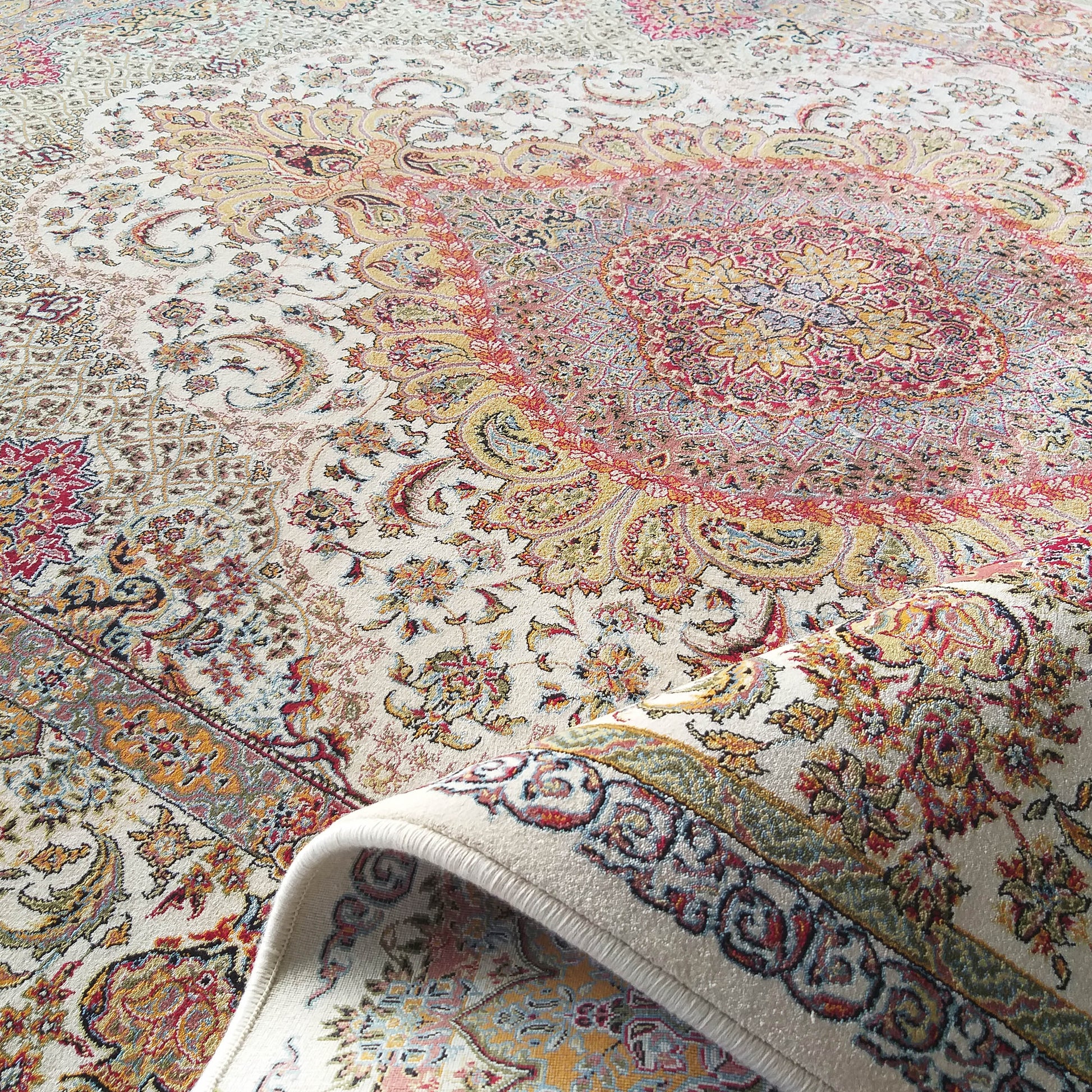 Tapis orné à fond crème et motifs complexes rouges, or et bleus Un coin du tapis est élégamment enroulé