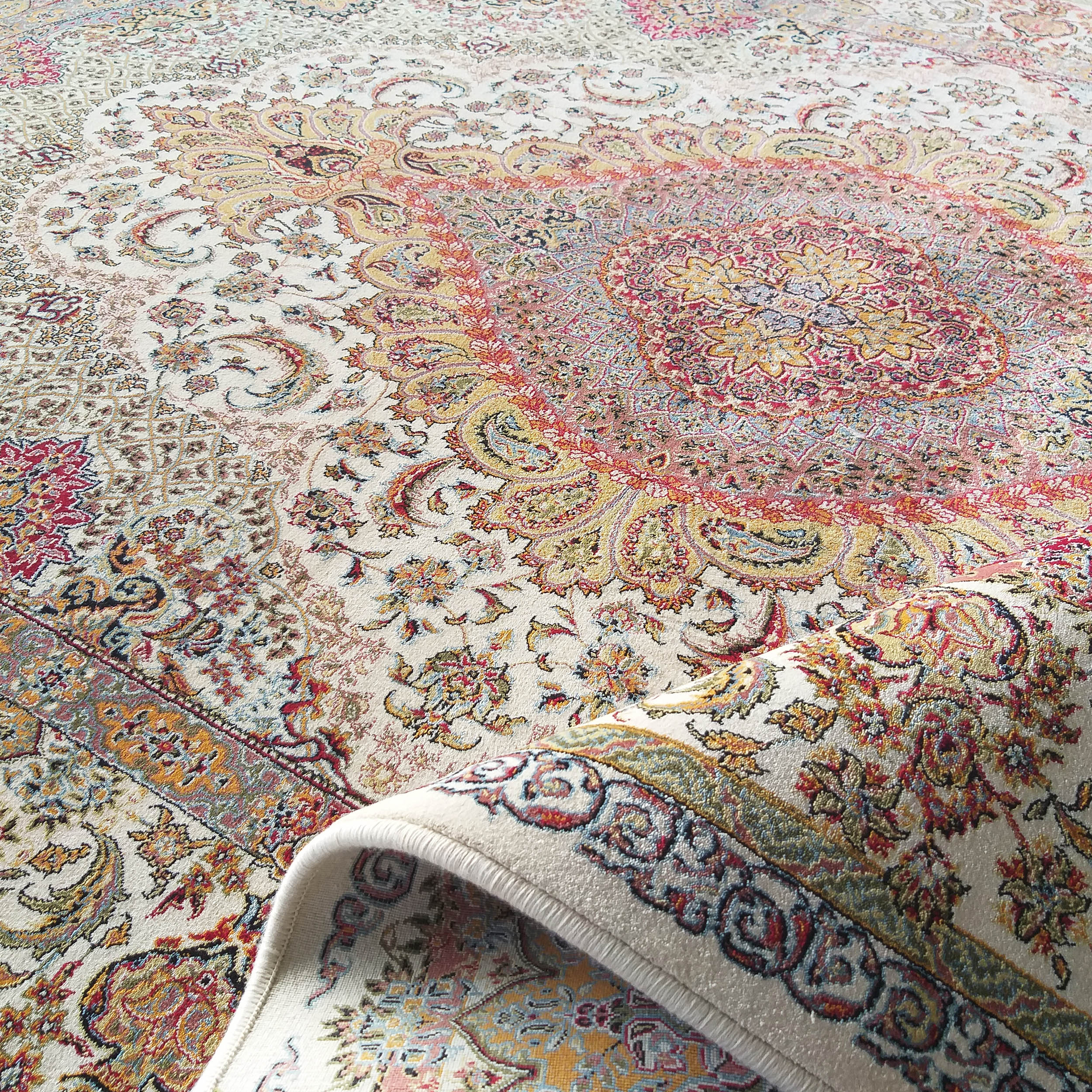 Tapis orné à fond crème et motifs complexes rouges, or et bleus Un coin du tapis est élégamment enroulé