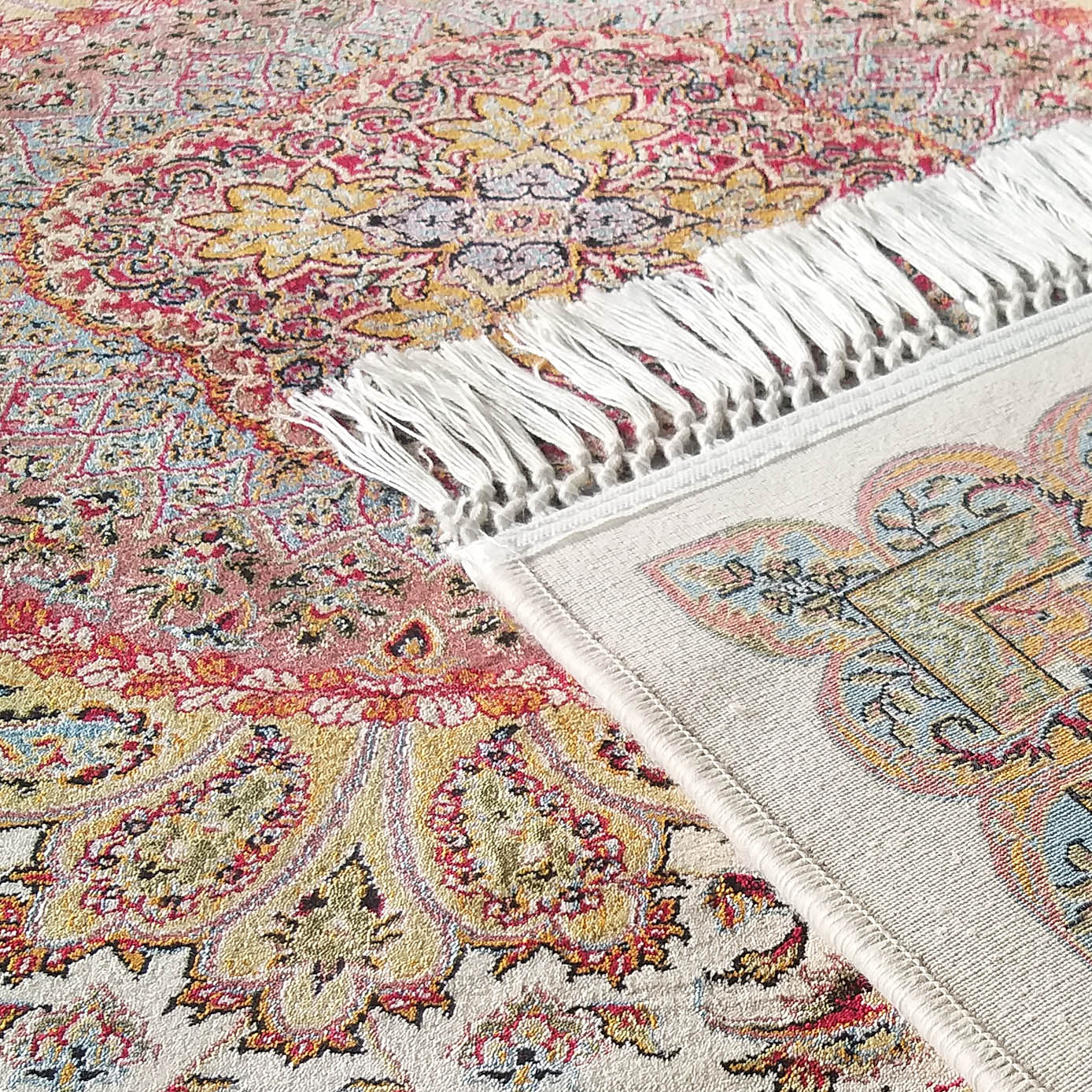 Tapis crème à la texture douce, avec des motifs floraux et cachemire colorés et des franges blanches, posé sur un tapis similaire