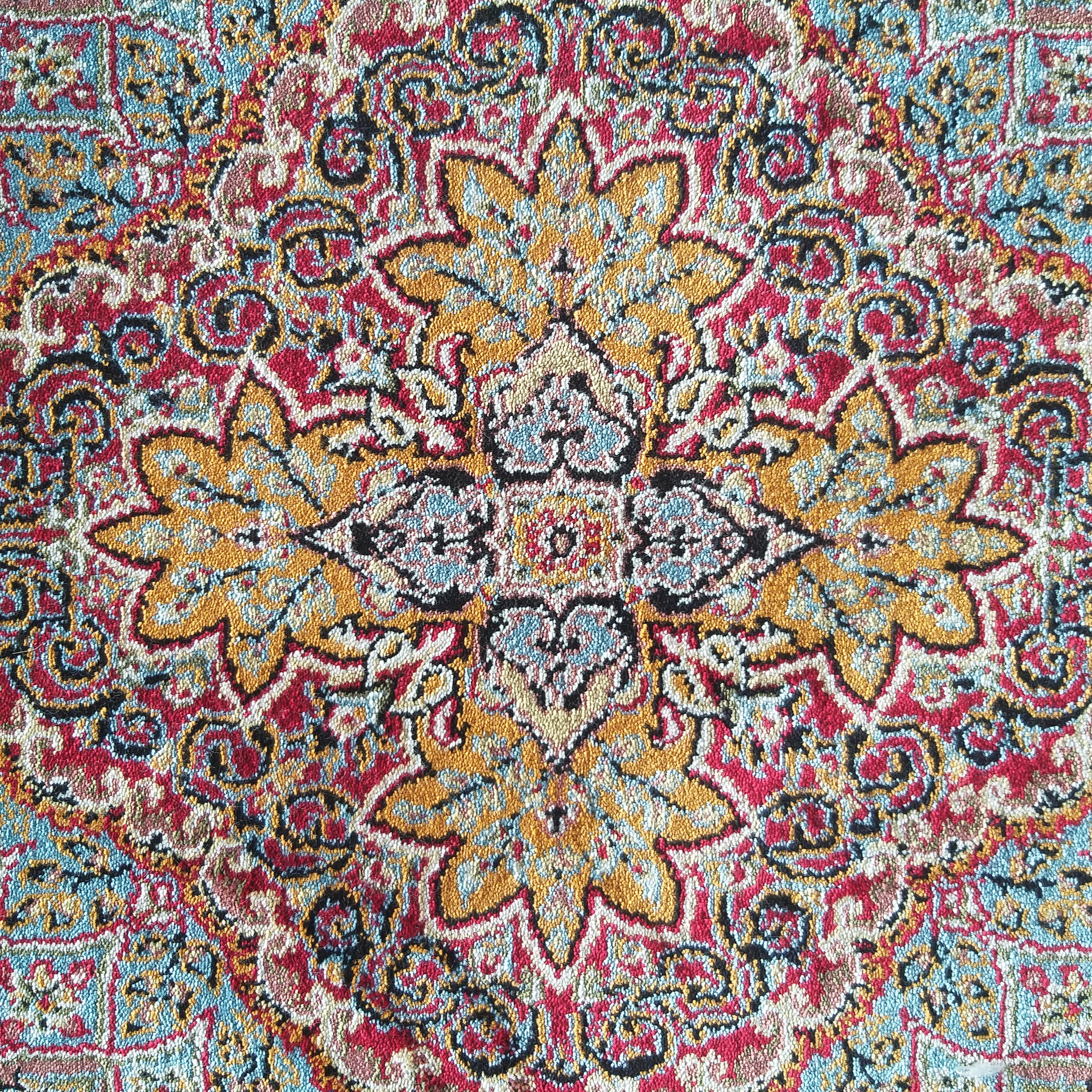 Tapis en tissu coloré aux motifs orientaux complexes, dominé par le rouge, l'or, le bleu clair et le noir