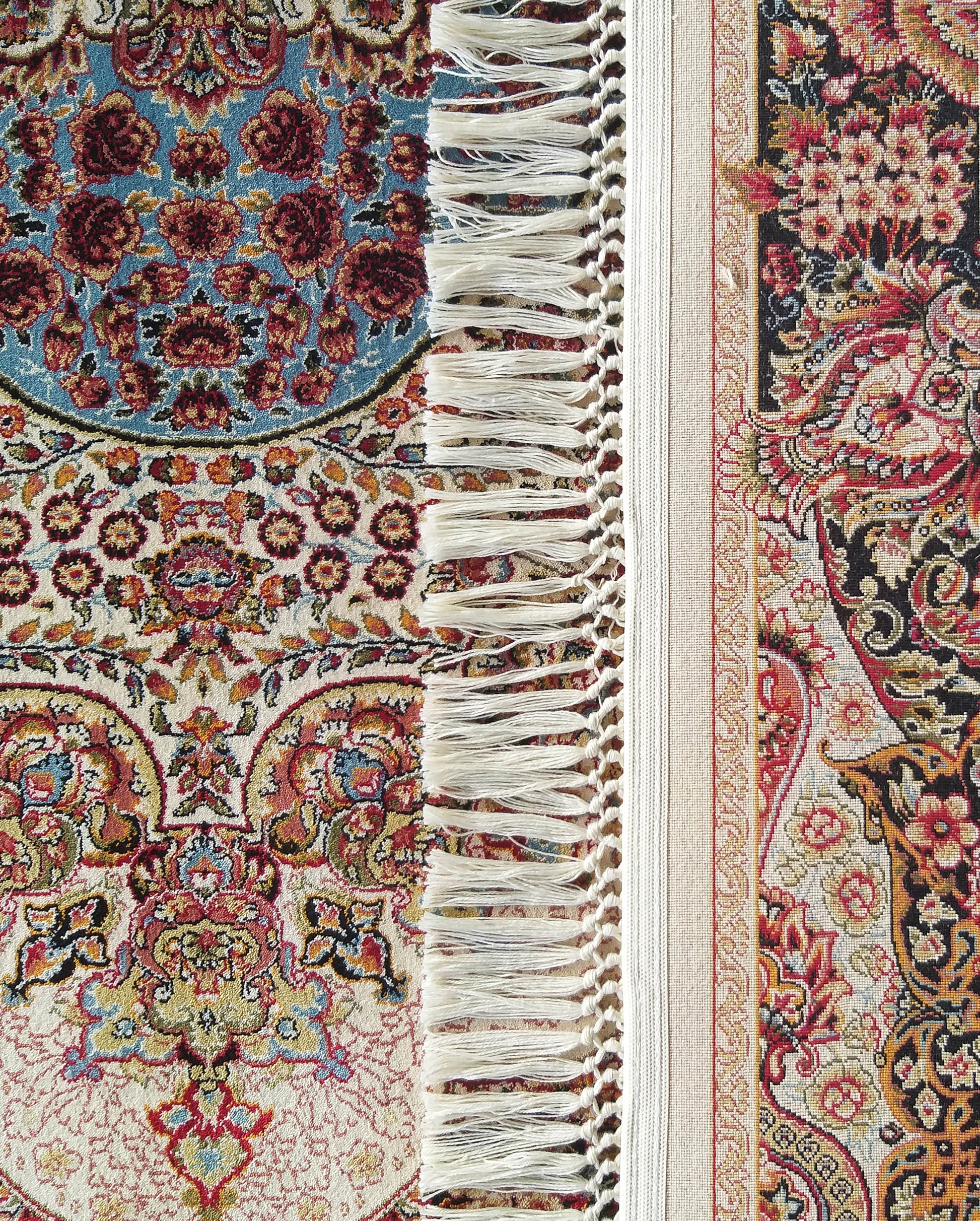 Tapis textile aux motifs floraux et ornementaux complexes rouges, bleus, noirs, crème et dorés, avec des franges claires