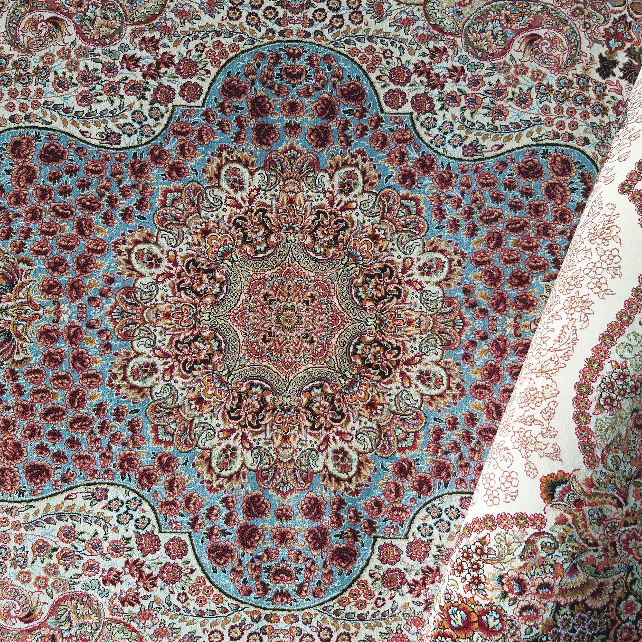 Tapis enroulé d'un côté, avec des motifs floraux et un médaillon central en bleu, rouge et crème