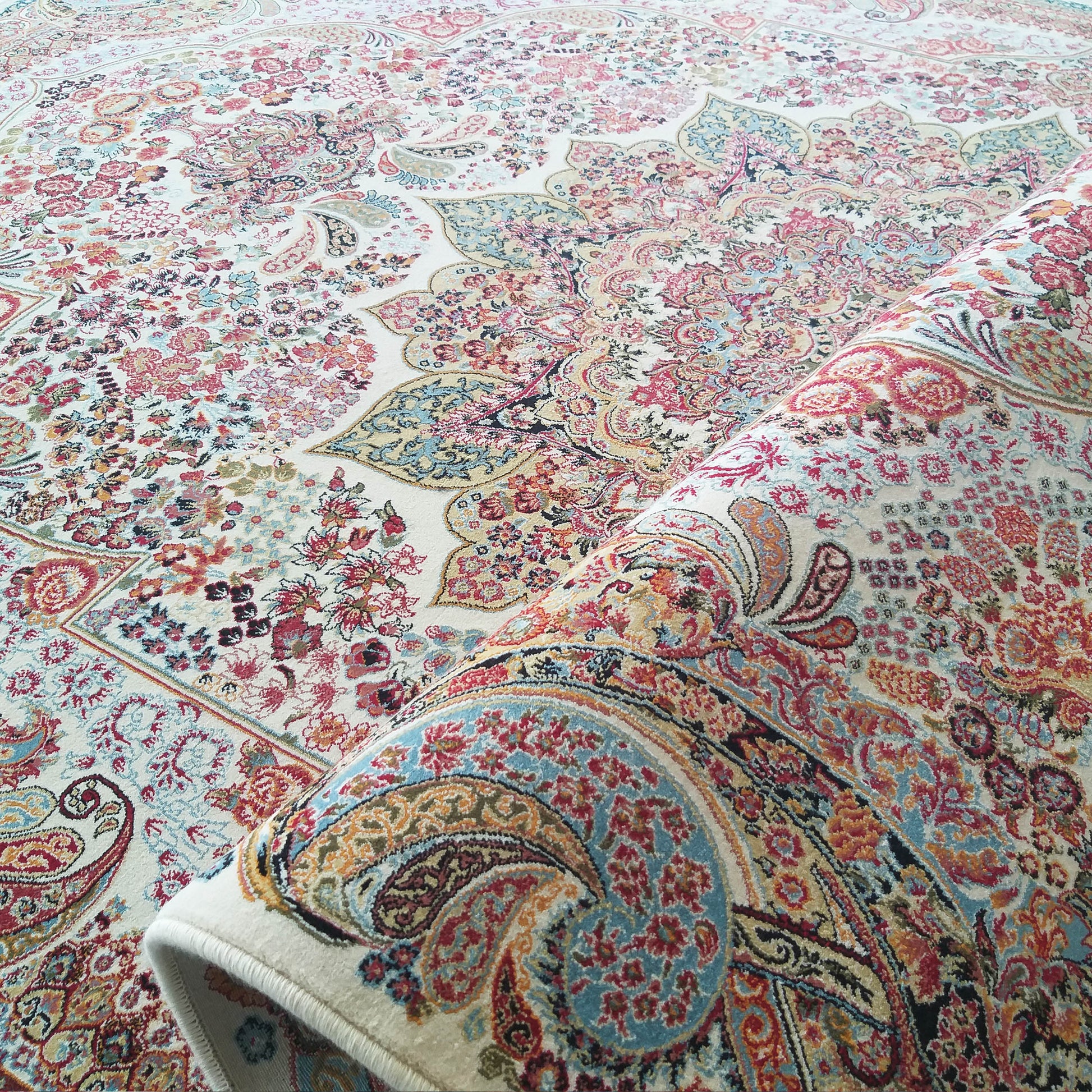 Tapis aux riches motifs floraux et cachemire multicolores sur fond crème, partiellement roulé sur le côté