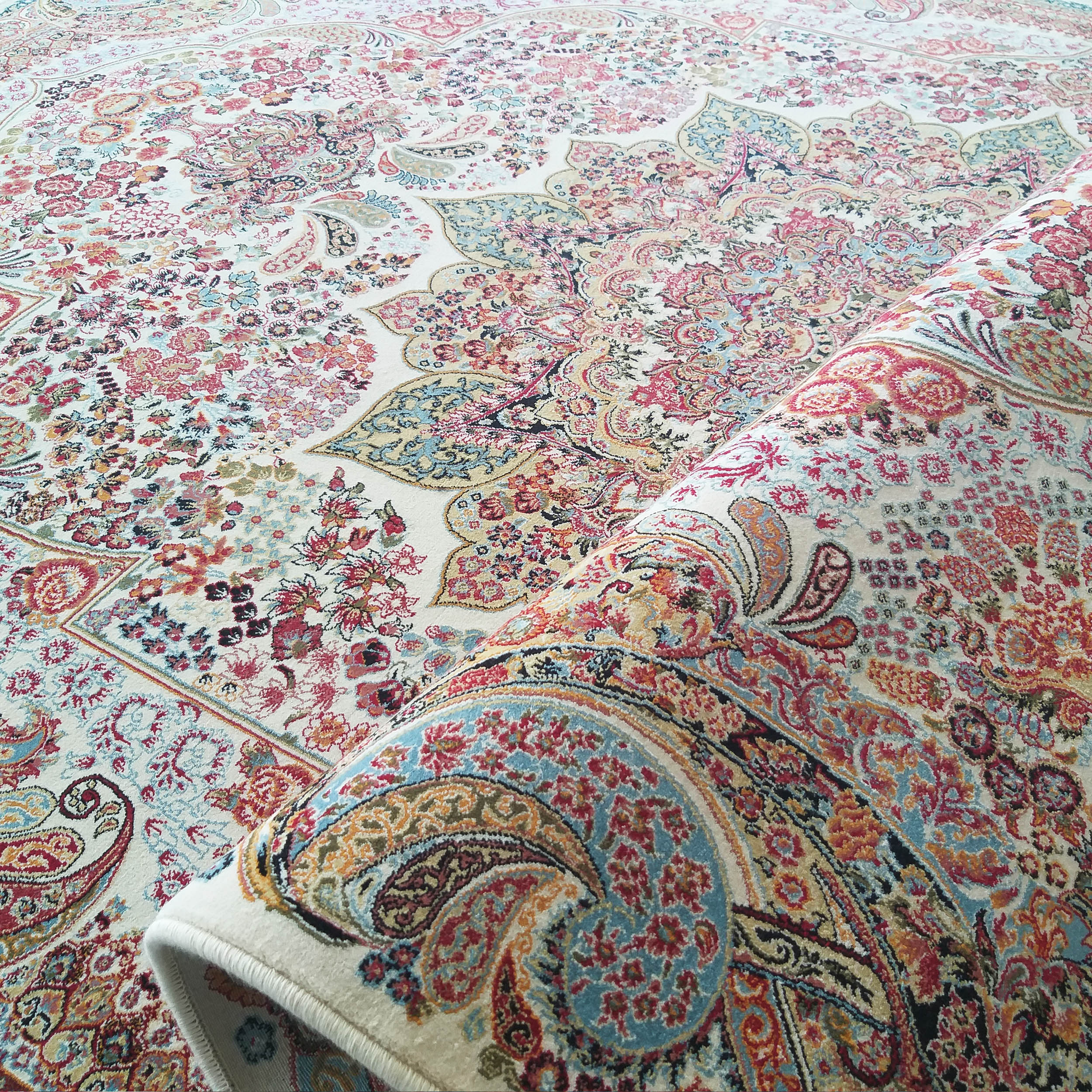 Tapis aux riches motifs floraux et cachemire multicolores sur fond crème, partiellement roulé sur le côté